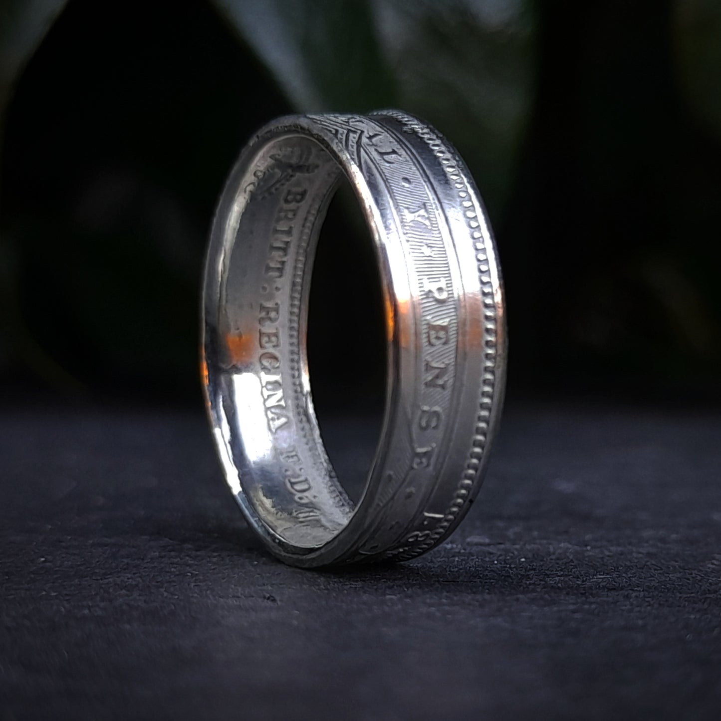 The 1800s Victorian Shilling Ring by silverhollowjewellery is a handmade sterling silver accessory that stands upright on a dark surface, highlighting its detailed engravings and inscriptions along the edge and inner band.