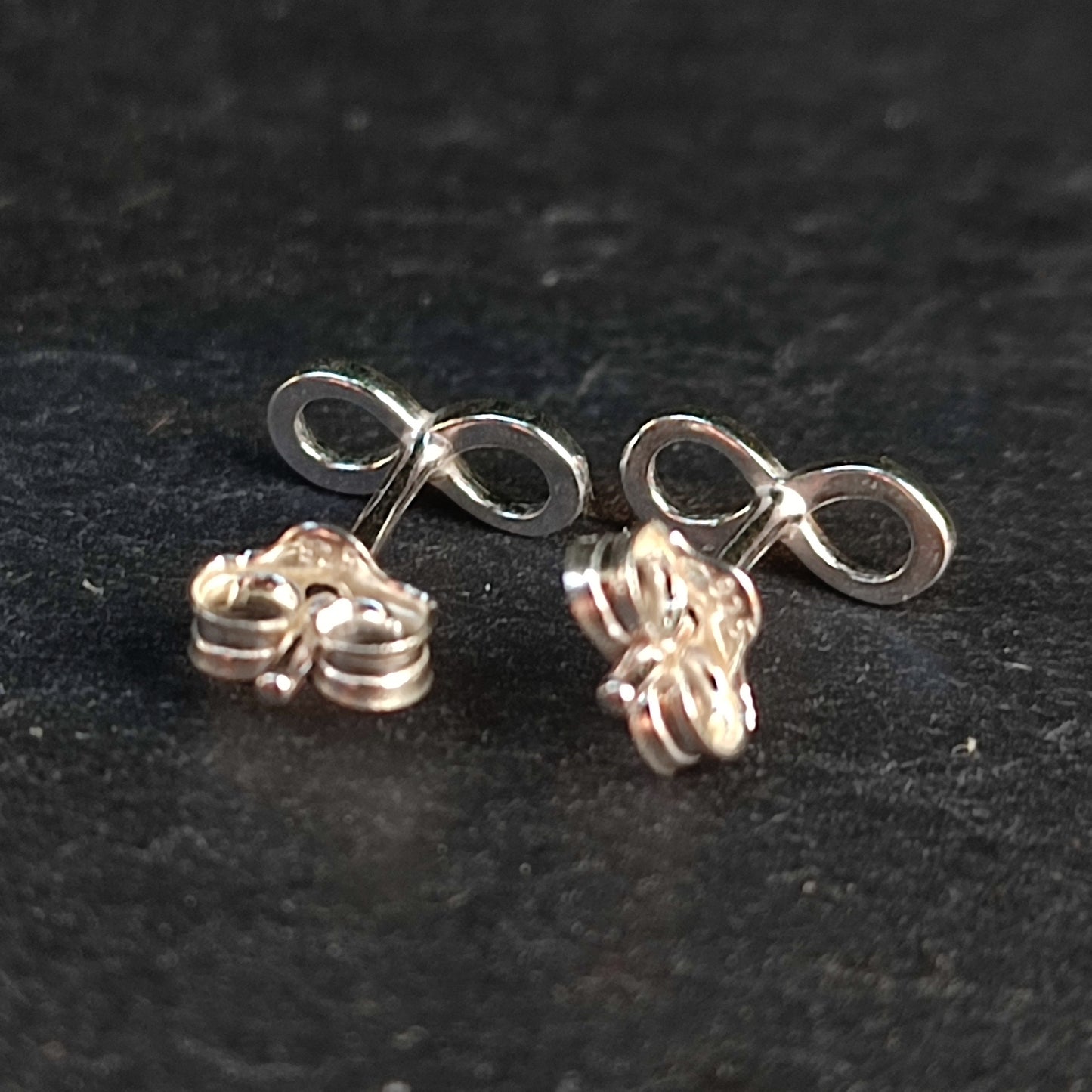 Infinity Stud Earrings- Sterling Silver by silverhollowjewellery, featuring 925 sterling silver and butterfly backs, displayed on a dark surface.