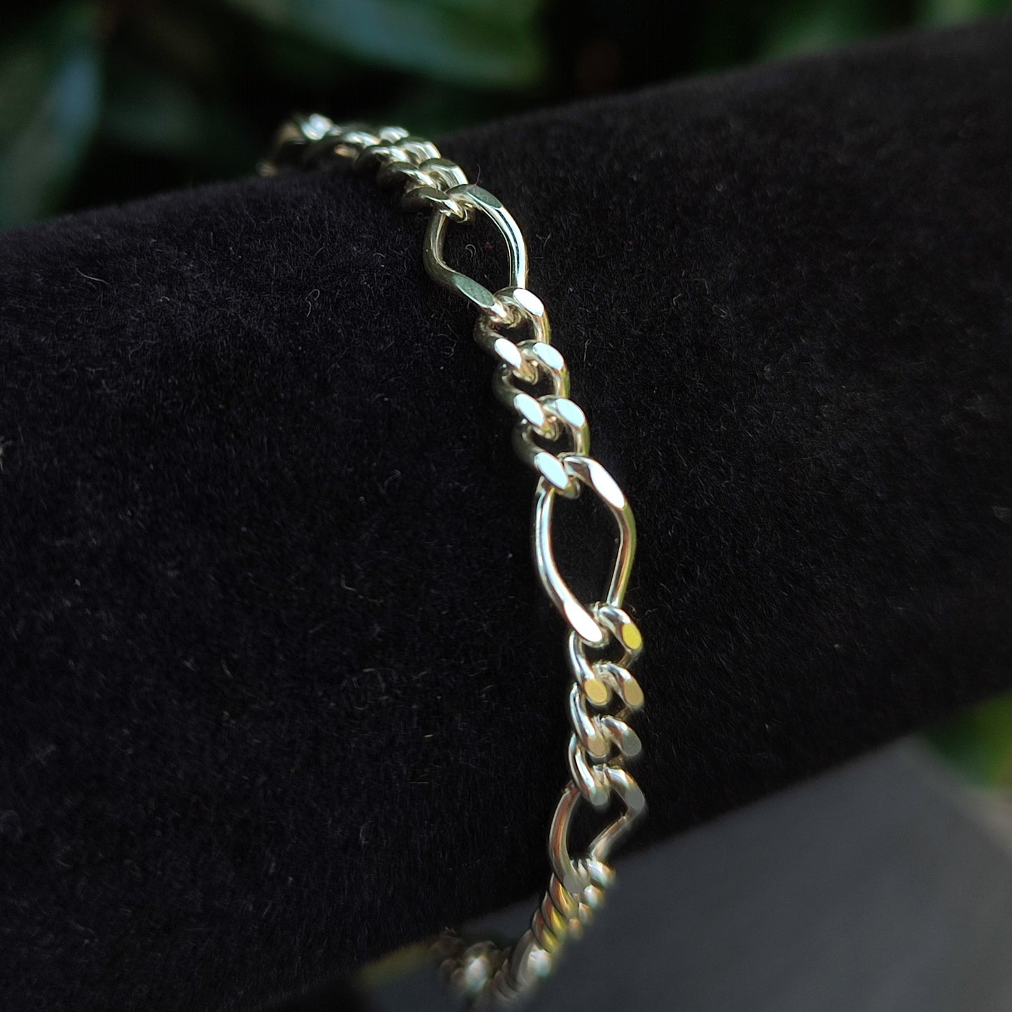 The silverhollowjewellery Figaro Chain Bracelet in sterling silver features elongated oval and round links, elegantly presented on a black velvet roll.