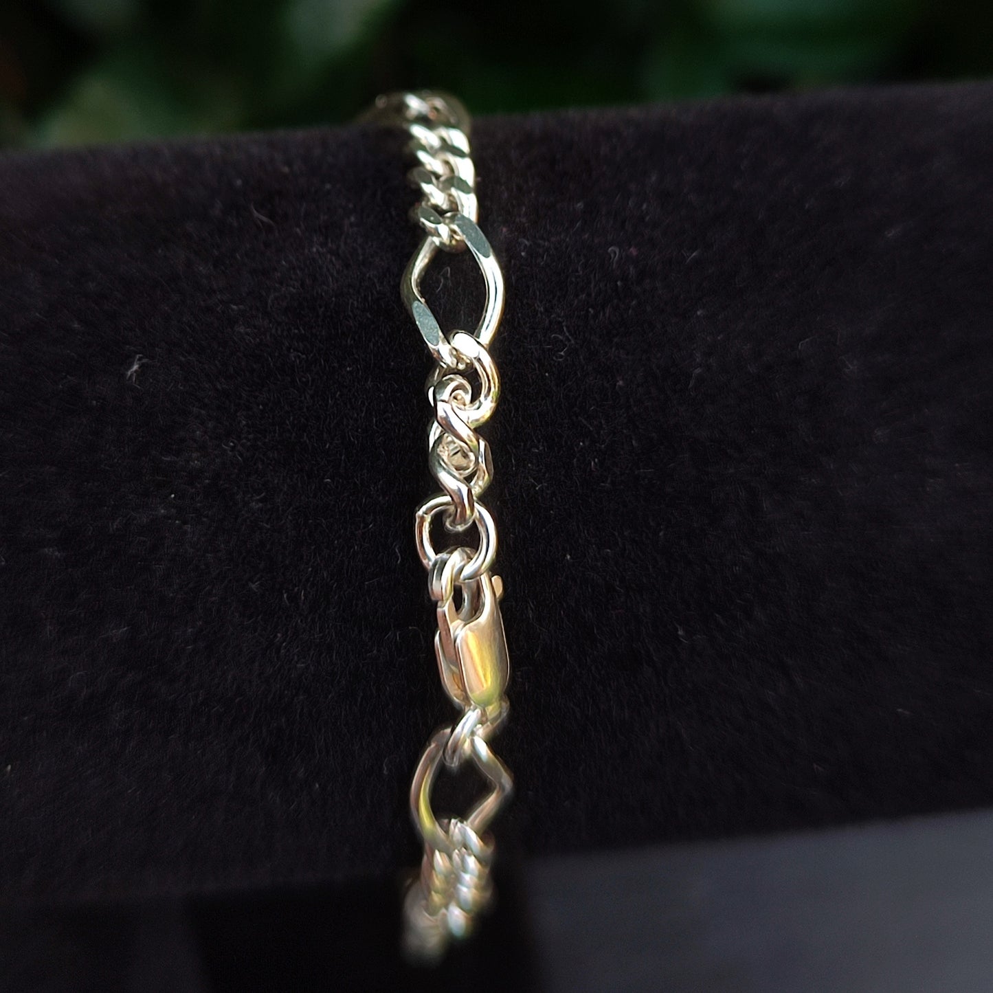 A close-up of the silverhollowjewellery Figaro Chain Bracelet in sterling silver, showcasing its lobster clasp and diamond-cut links, displayed on black velvet.