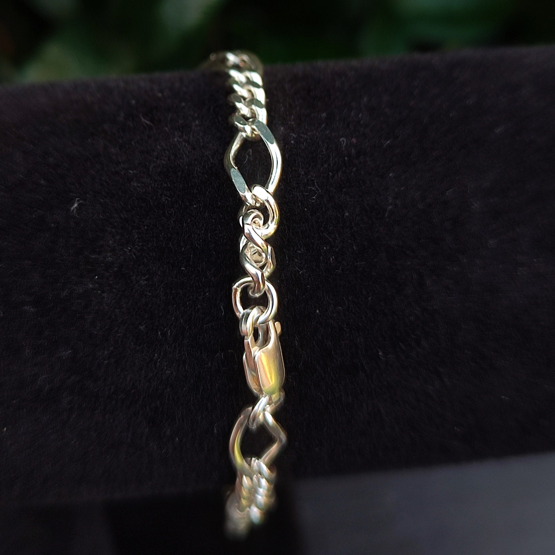 A close-up of the silverhollowjewellery Figaro Chain Bracelet in sterling silver, showcasing its lobster clasp and diamond-cut links, displayed on black velvet.