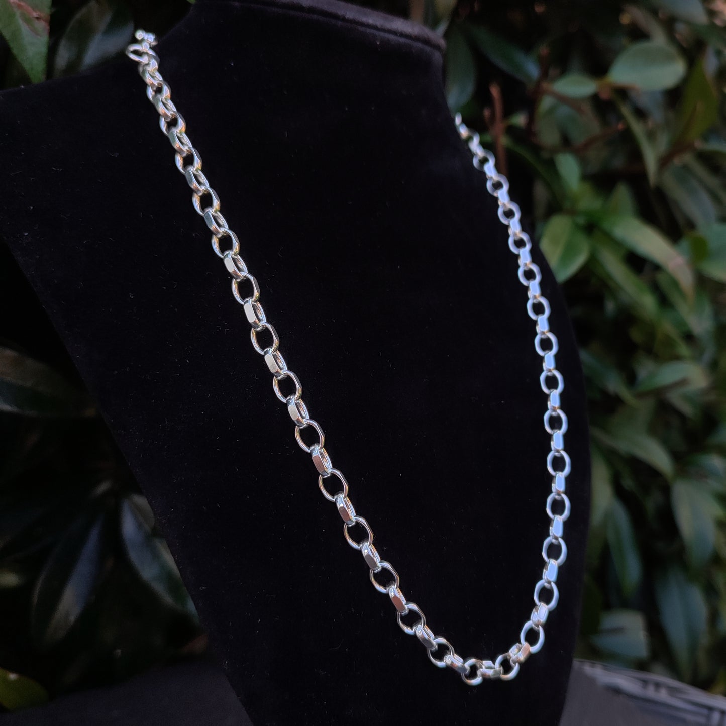 The silverhollowjewellery Heavy Belcher Chain Necklace in sterling silver is displayed on a black velvet stand, set against a backdrop of green foliage.