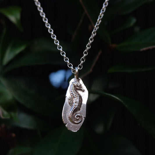 The silverhollowjewellery Seahorse Pendant Sterling Silver necklace is handcrafted from recycled 925 sterling silver and features an engraved seahorse design set against a background of green leaves.