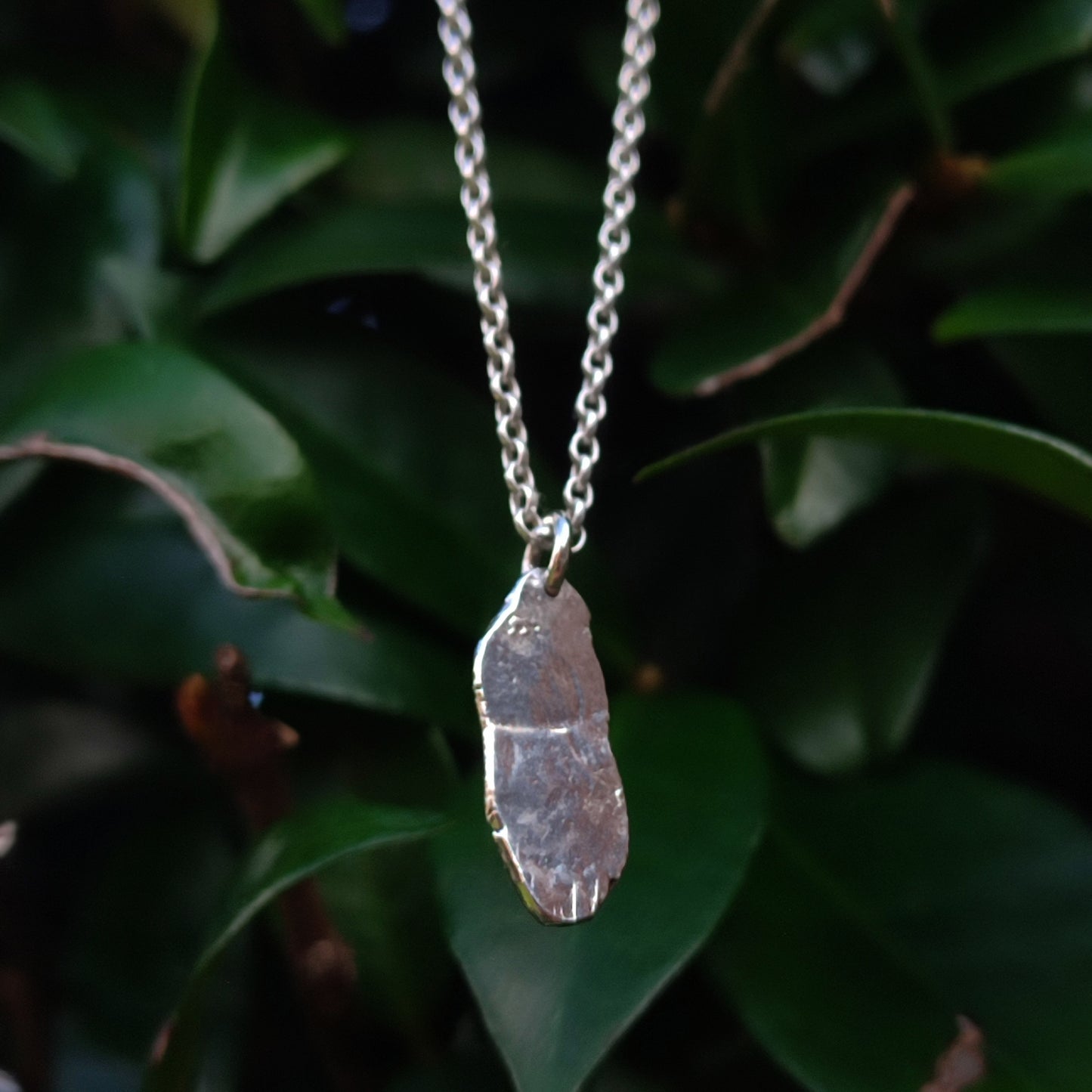 A handcrafted Seahorse Pendant in recycled 925 sterling silver by silverhollowjewellery, displayed against green leaves.