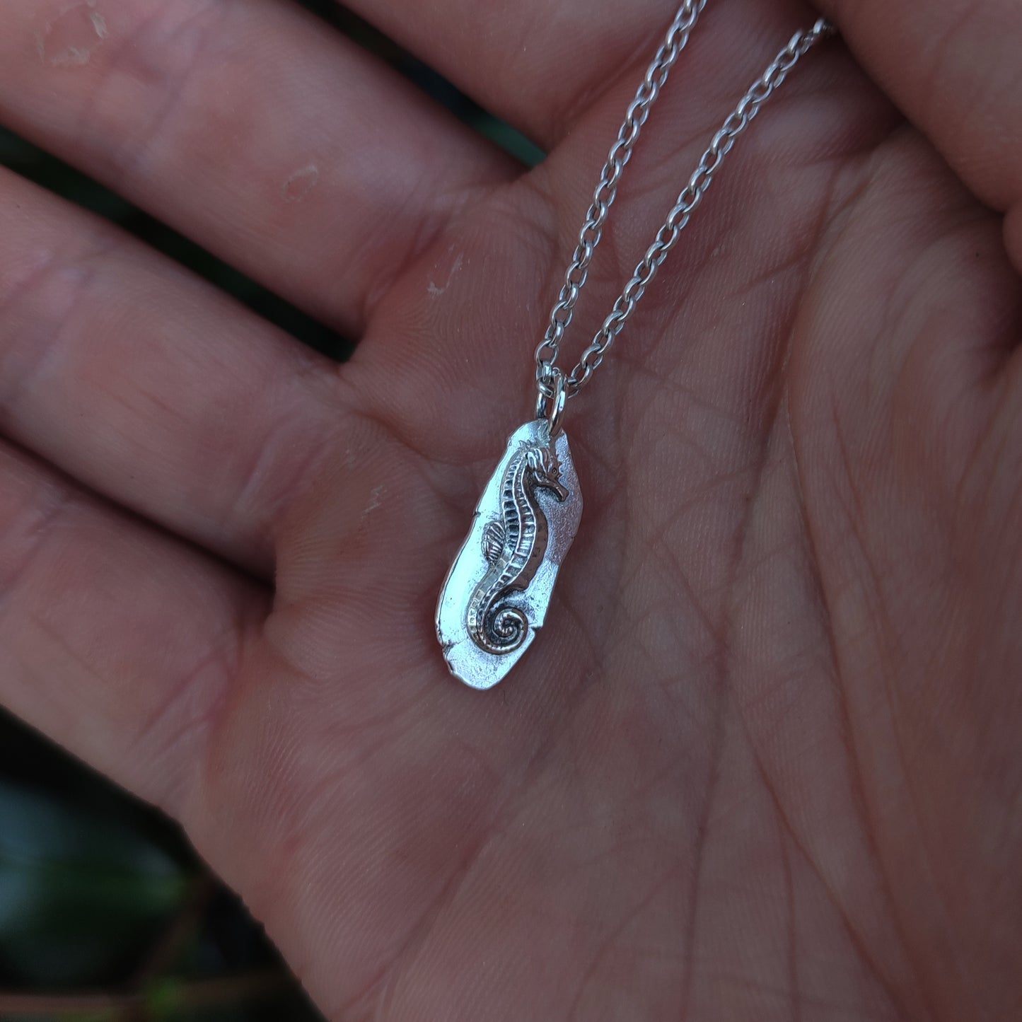 A close-up shows a hand holding the silverhollowjewellery Seahorse Pendant Sterling Silver, beautifully engraved and crafted from recycled 925 sterling silver.