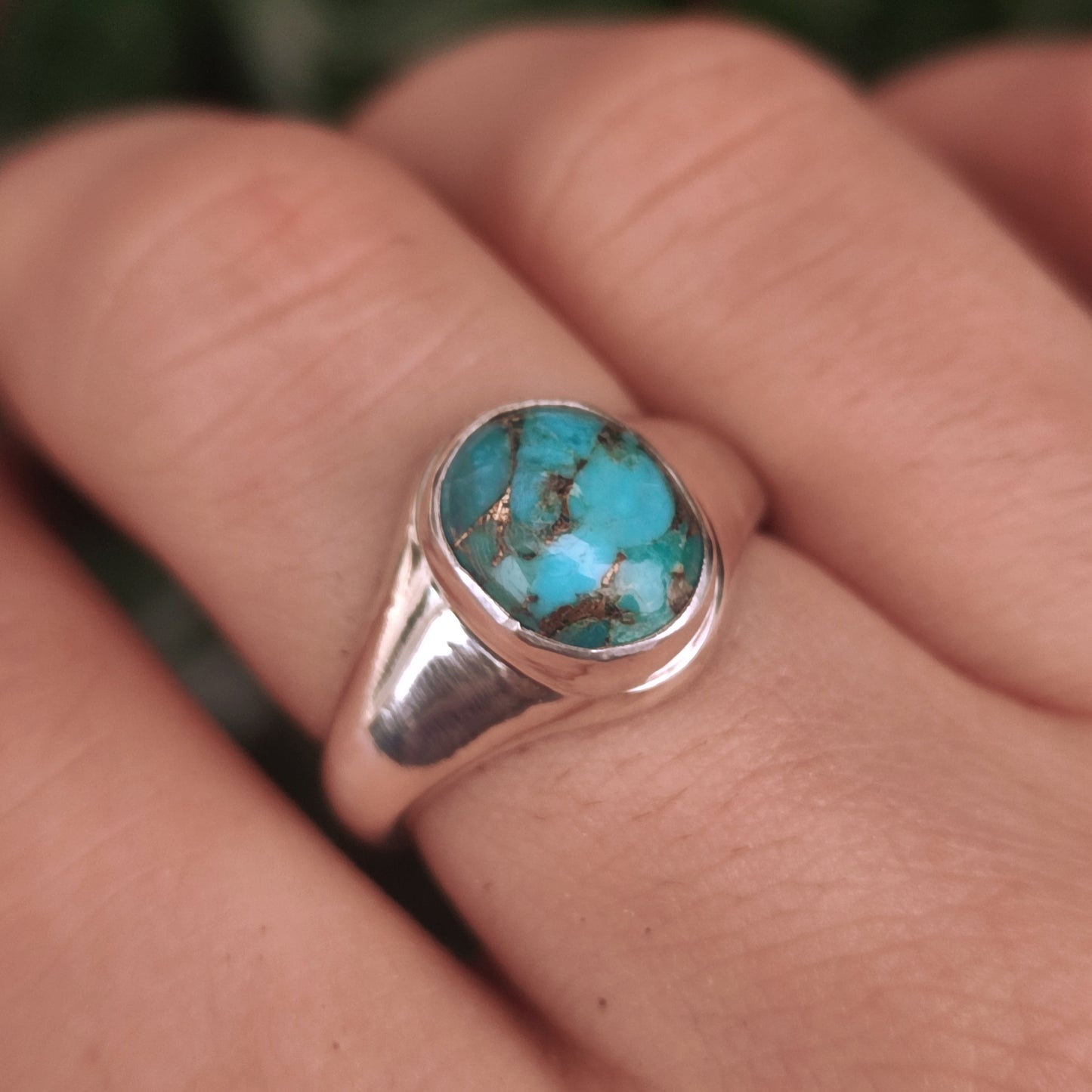A hand wears the Turquoise Signet Ring-Sterling Silver by silverhollowjewellery, featuring an ethically sourced oval turquoise gemstone with distinctive brown matrix patterns.