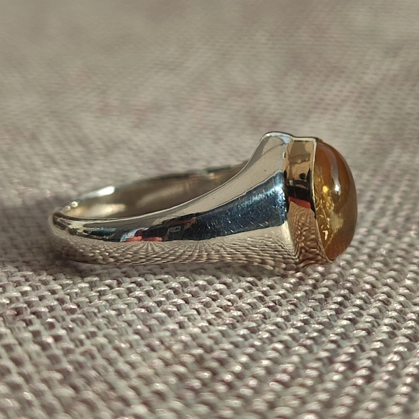 The Gold Bezel Citrine Ring by silverhollowjewellery features a smooth, rounded citrine gemstone set in a gold-tone bezel—a stunning piece of handcrafted jewelry displayed on textured fabric.