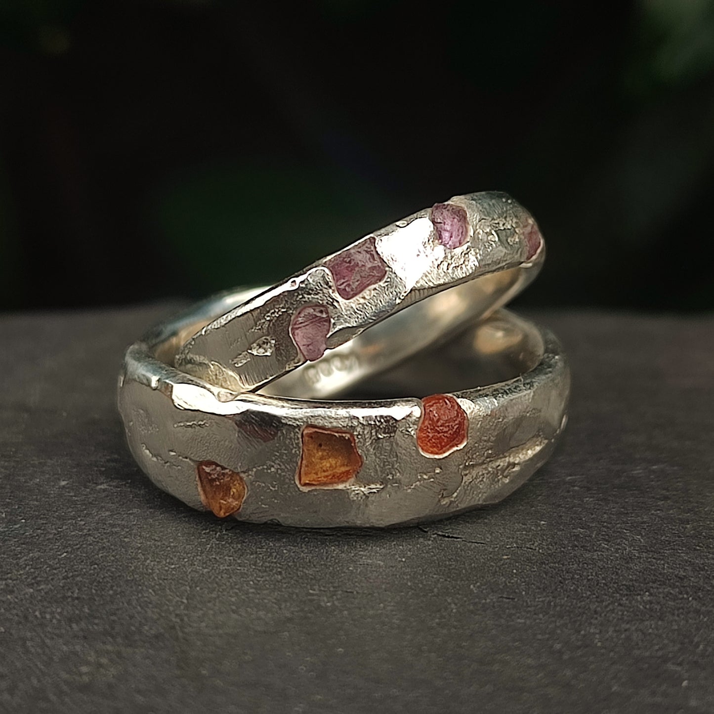 Two Raw Sapphire Band Sterling Silver rings by silverhollowjewellery, featuring hammered recycled sterling silver set with small, irregular sapphires, are displayed against a dark blurred background.