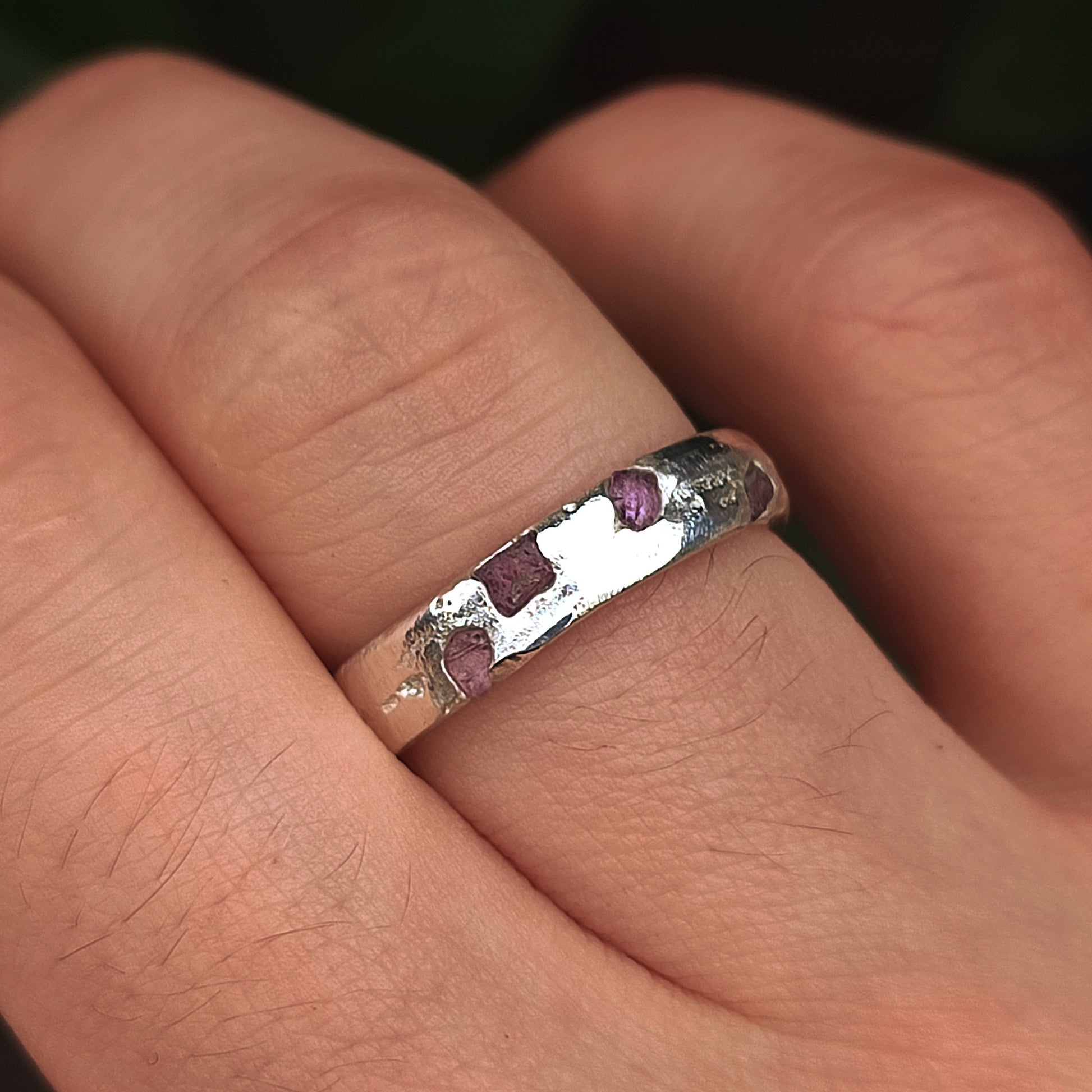 A close-up of a hand wearing the silverhollowjewellery Raw Sapphire Band Sterling Silver-Custom, set with small purple raw sapphire gemstones.