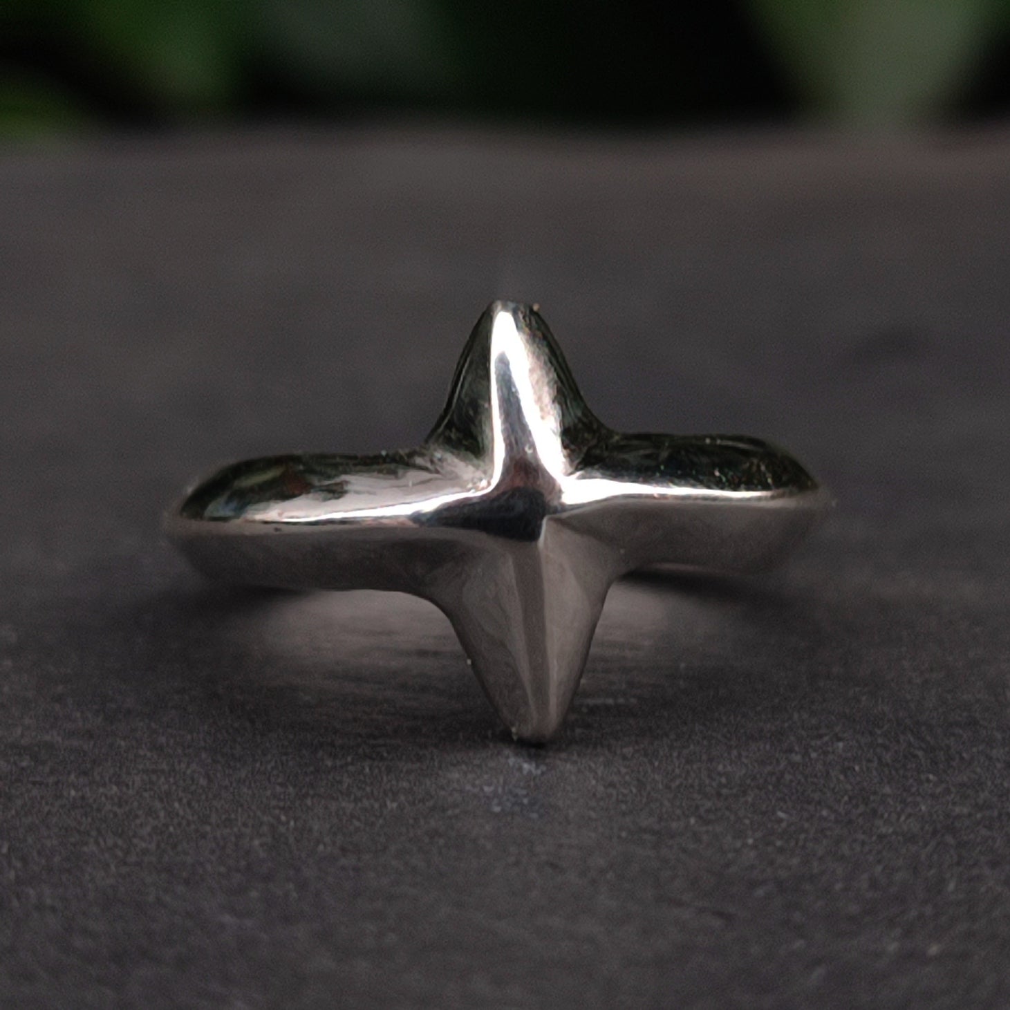 The North Star Ring Sterling Silver by silverhollowjewellery features a handcrafted, raised four-pointed geometric design at the center, elegantly displayed on a dark surface.