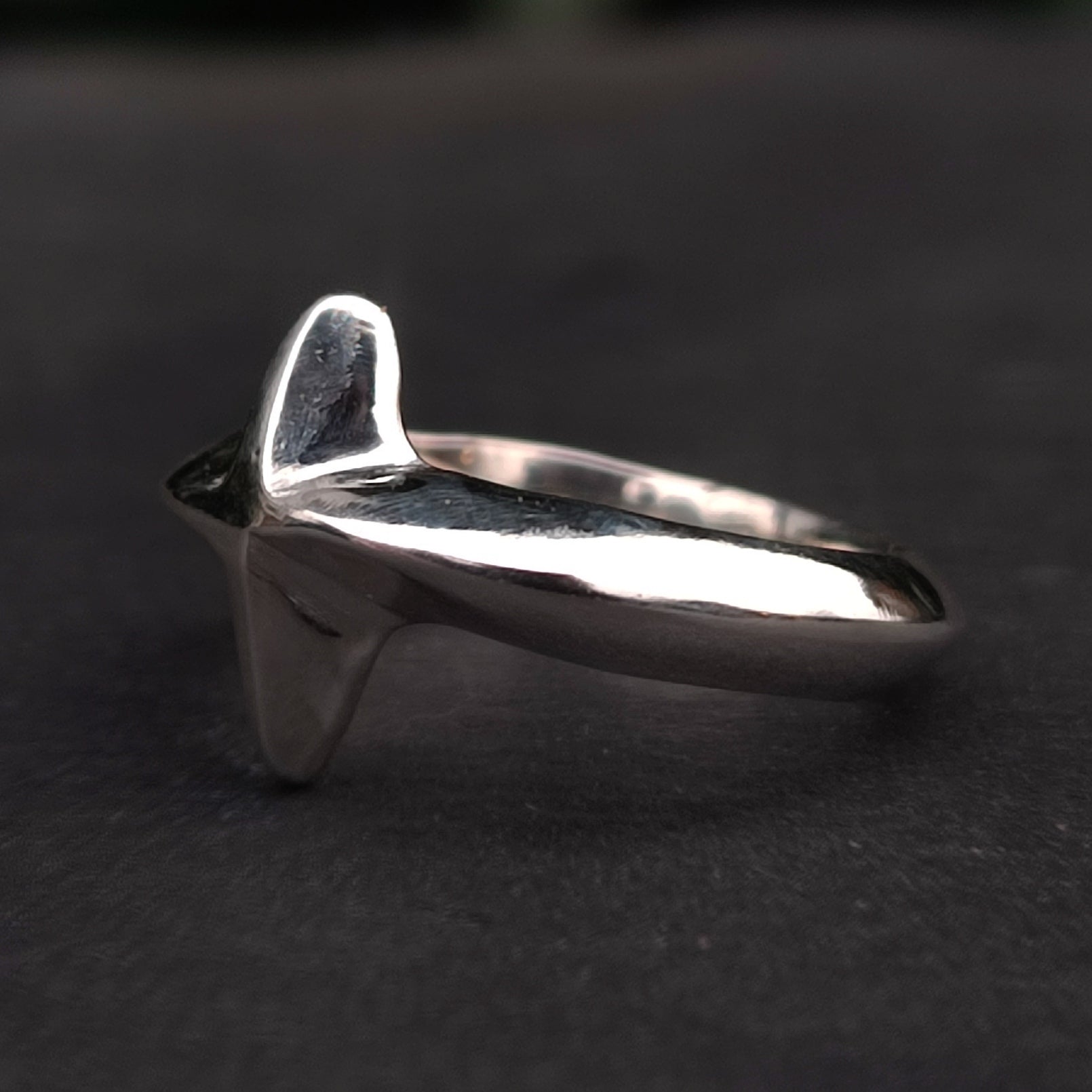 The North Star Ring Sterling Silver by silverhollowjewellery is a handcrafted, unisex ring with a sculpted shark fin design, adding a bold, modern accent to any style. Seen here on a dark surface.