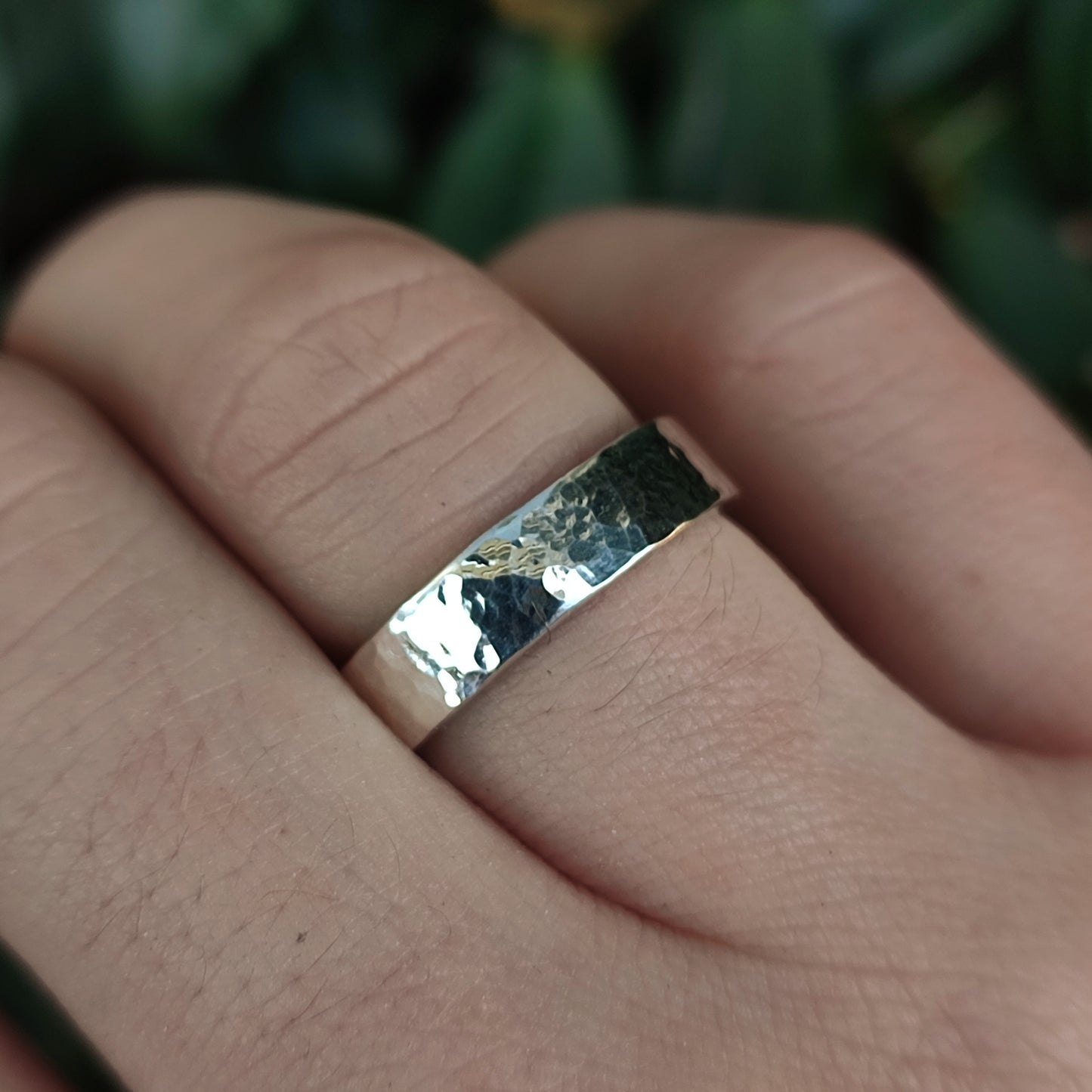 A hand wears the Chunky Hammered Ring Sterling Silver by silverhollowjewellery, crafted from recycled 925 sterling silver, with a blurred green background.