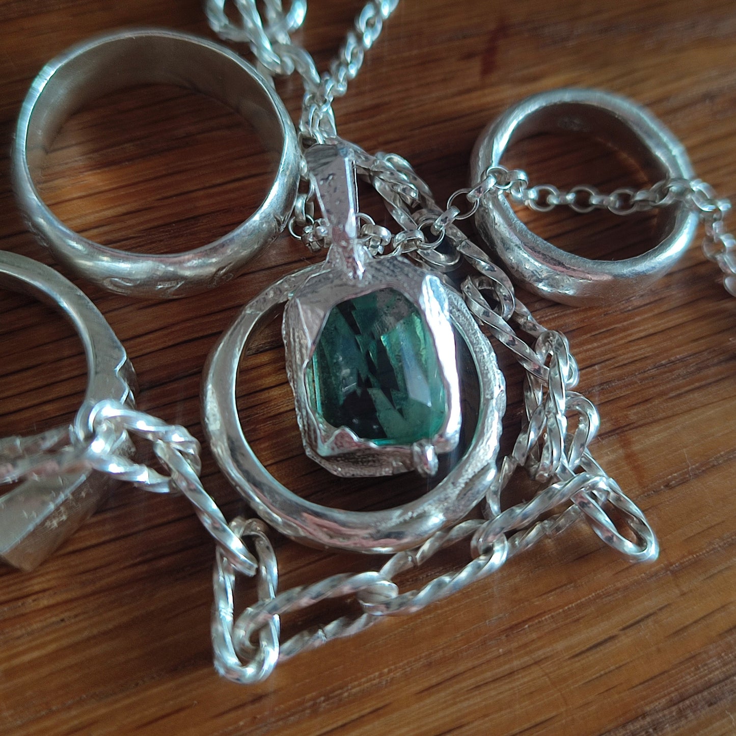 Several sterling silver rings and the silverhollowjewellery Feather Teal Sapphire Pendant in sterling silver are displayed on a wooden surface.