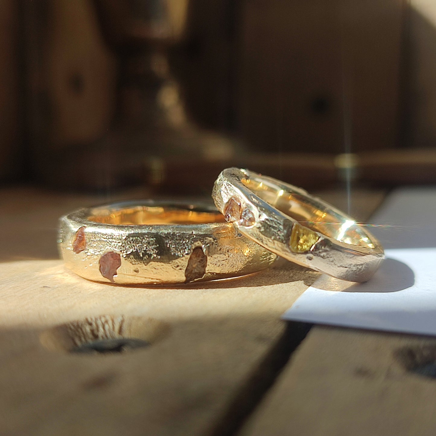 The Raw Sapphire Band 9ct Gold by silverhollowjewellery features a rustic, hammered texture and rests on a wooden surface in natural sunlight.