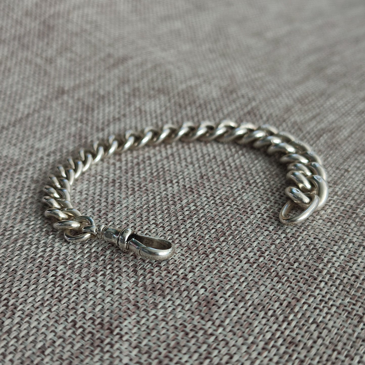 The Silver Watch Chain Bracelet by silverhollowjewellery, featuring a sterling silver antique-style curb chain and lobster clasp, is displayed on a textured fabric surface.