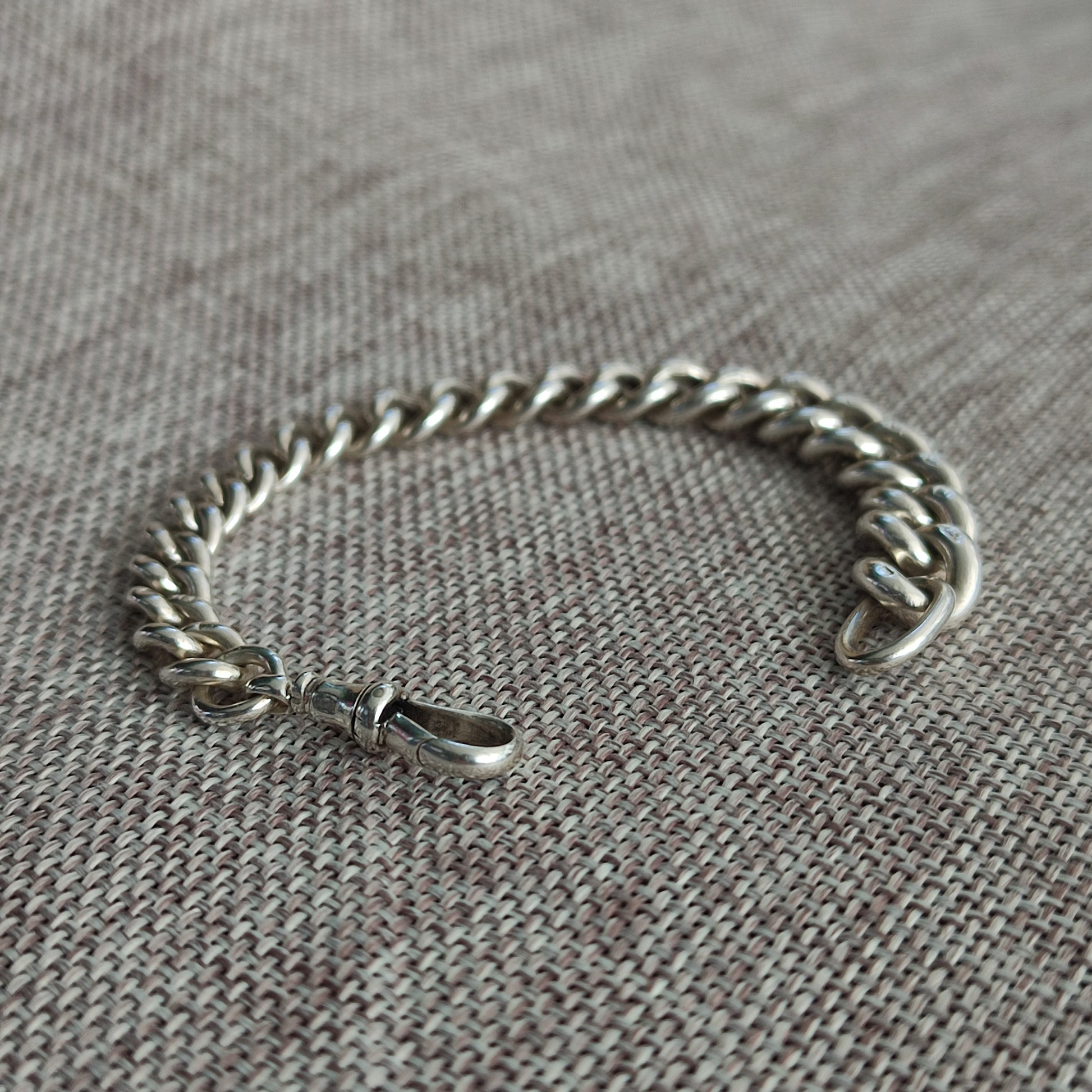 The Silver Watch Chain Bracelet by silverhollowjewellery, featuring a sterling silver antique-style curb chain and lobster clasp, is displayed on a textured fabric surface.
