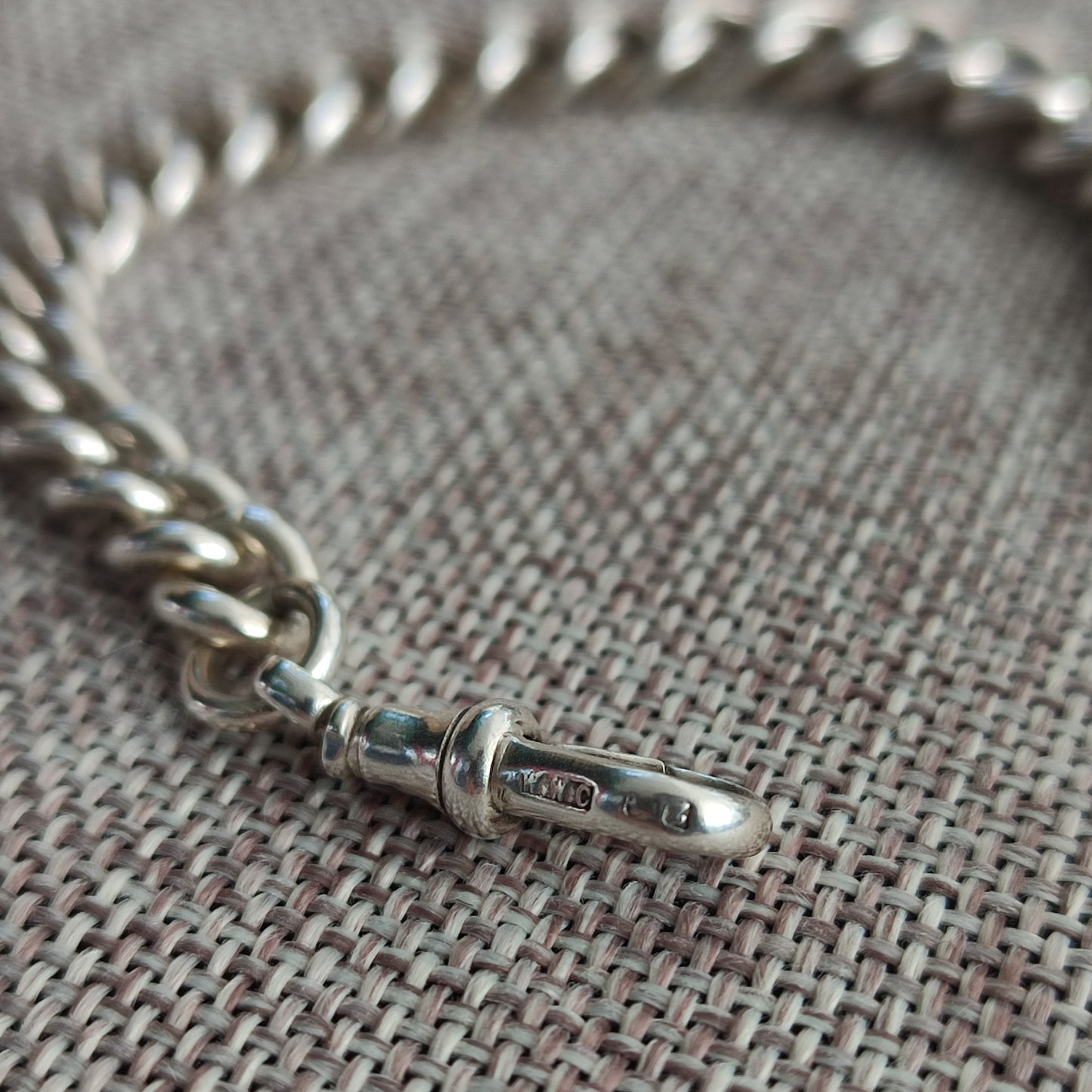 A close-up of the silverhollowjewellery Silver Watch Chain Bracelet with a clasp, displayed on a textured woven surface.
