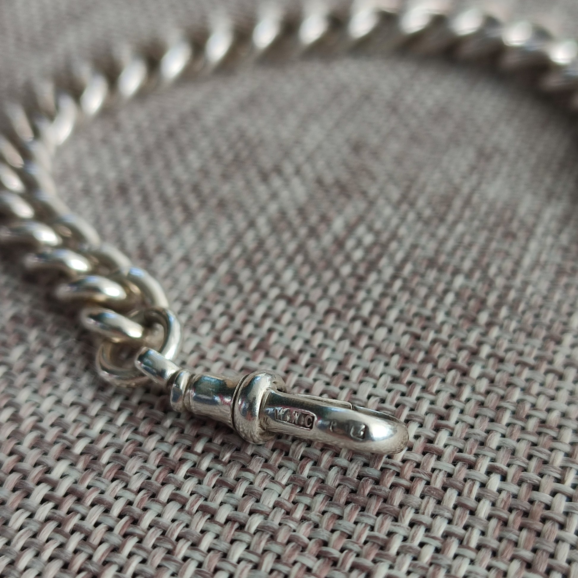 A close-up of the silverhollowjewellery Silver Watch Chain Bracelet with a clasp, displayed on a textured woven surface.