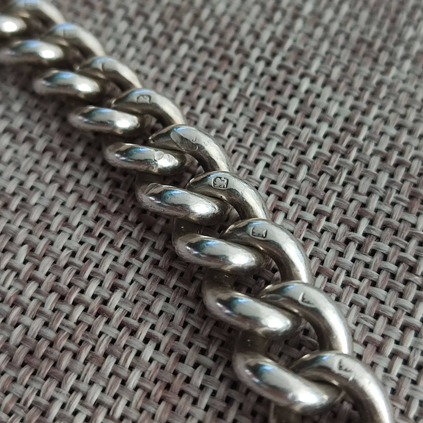 Close-up of a Silver Watch Chain Bracelet by silverhollowjewellery, featuring antique curb links and visible sterling silver hallmarks, displayed on textured woven fabric.