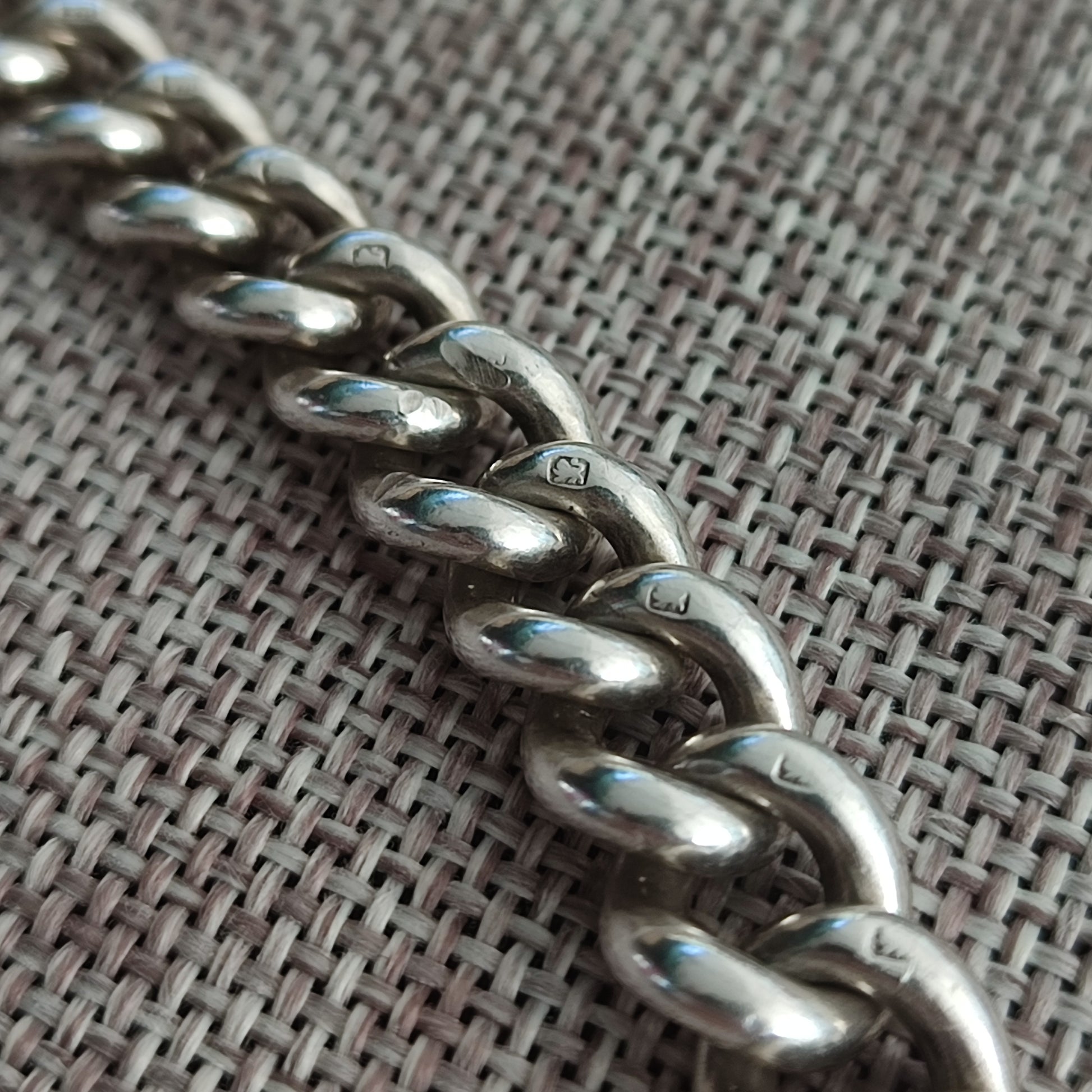 Close-up of a Silver Watch Chain Bracelet by silverhollowjewellery, featuring antique curb links and visible sterling silver hallmarks, displayed on textured woven fabric.