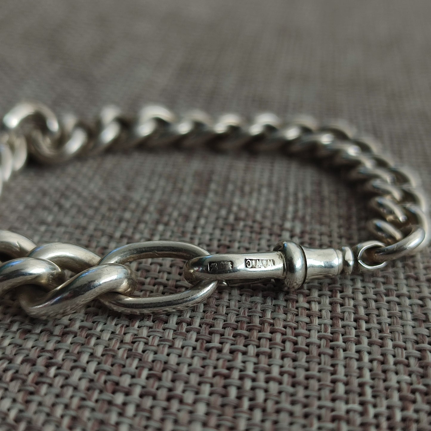 A close-up of the Silver Watch Chain Bracelet by silverhollowjewellery, featuring sterling silver with a clasp, displayed on textured fabric and evoking an antique curb chain style.