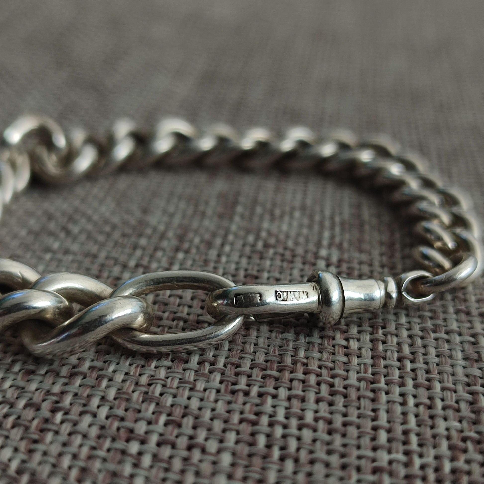 A close-up of the Silver Watch Chain Bracelet by silverhollowjewellery, featuring sterling silver with a clasp, displayed on textured fabric and evoking an antique curb chain style.