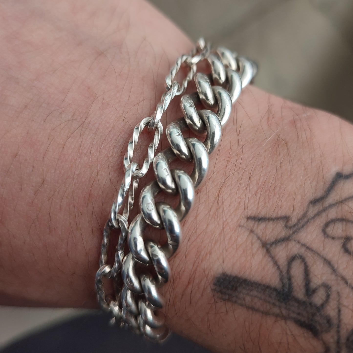 A close-up of a wrist adorned with the Silver Watch Chain Bracelet by silverhollowjewellery, paired with a black line tattoo featuring abstract shapes.