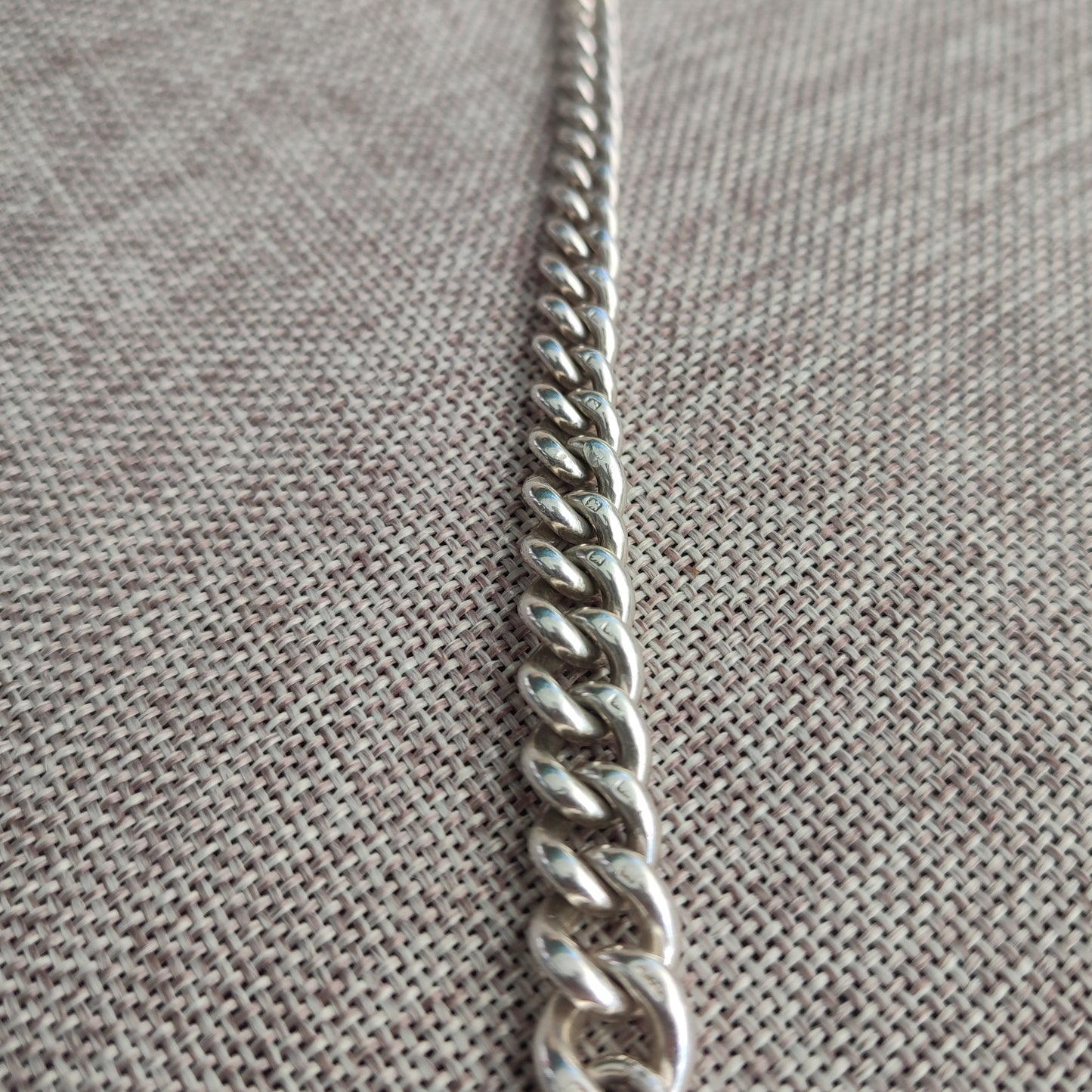 A close-up of the silverhollowjewellery Silver Watch Chain Bracelet, featuring an antique curb chain design, displayed on textured beige fabric.