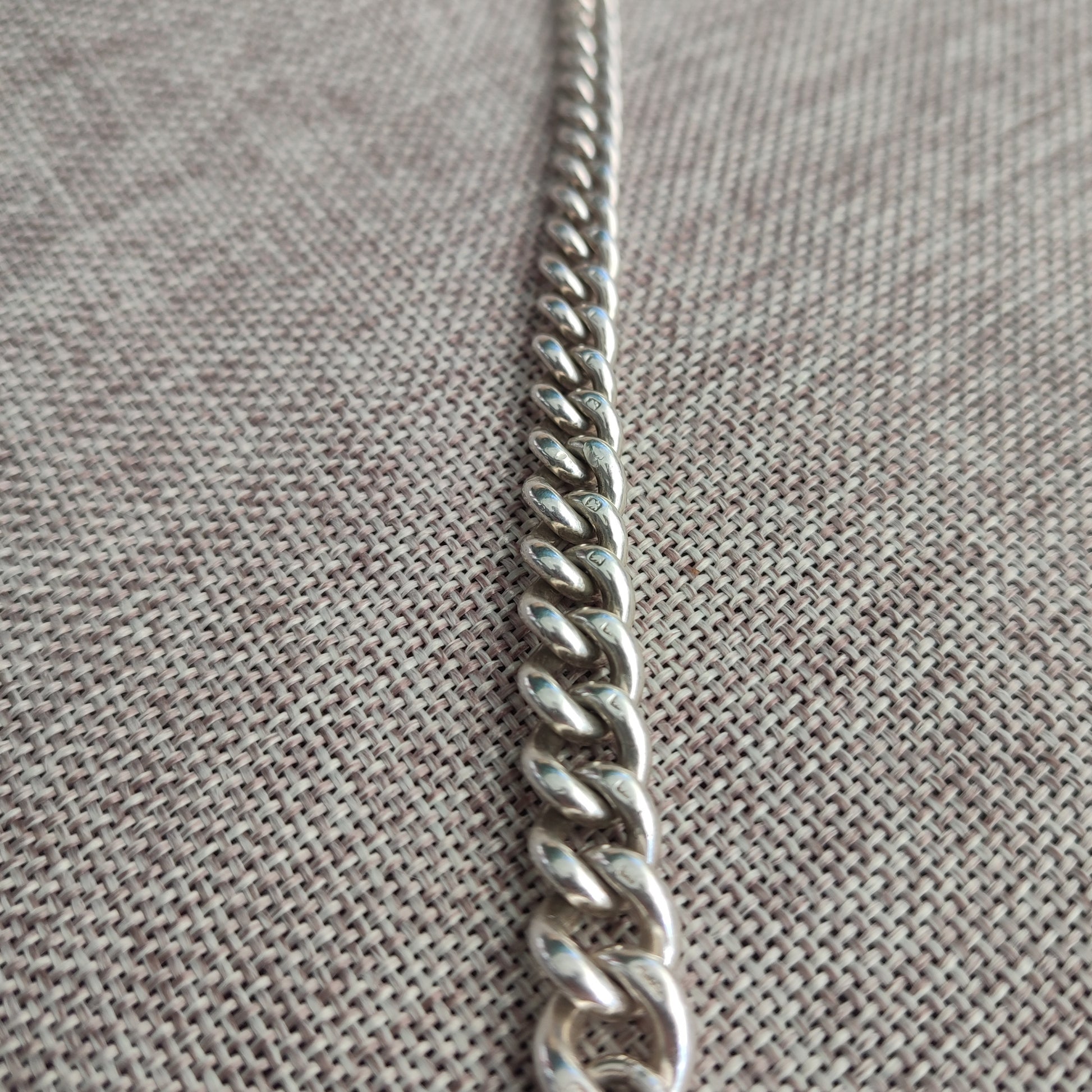 A close-up of the silverhollowjewellery Silver Watch Chain Bracelet, featuring an antique curb chain design, displayed on textured beige fabric.
