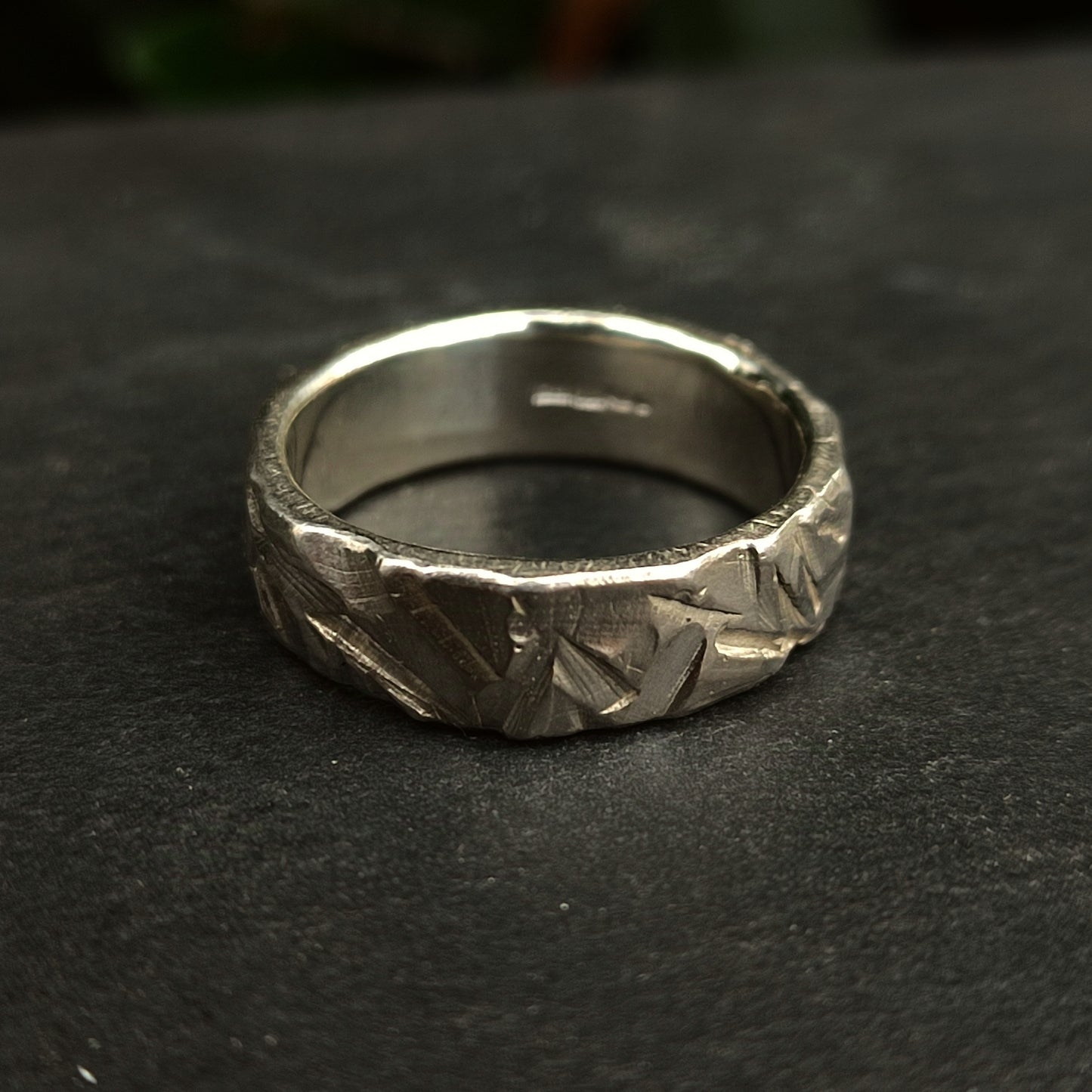 The Thick Rock Band by silverhollowjewellery, crafted in sterling silver with a hammered, textured finish, rests on a dark surface.