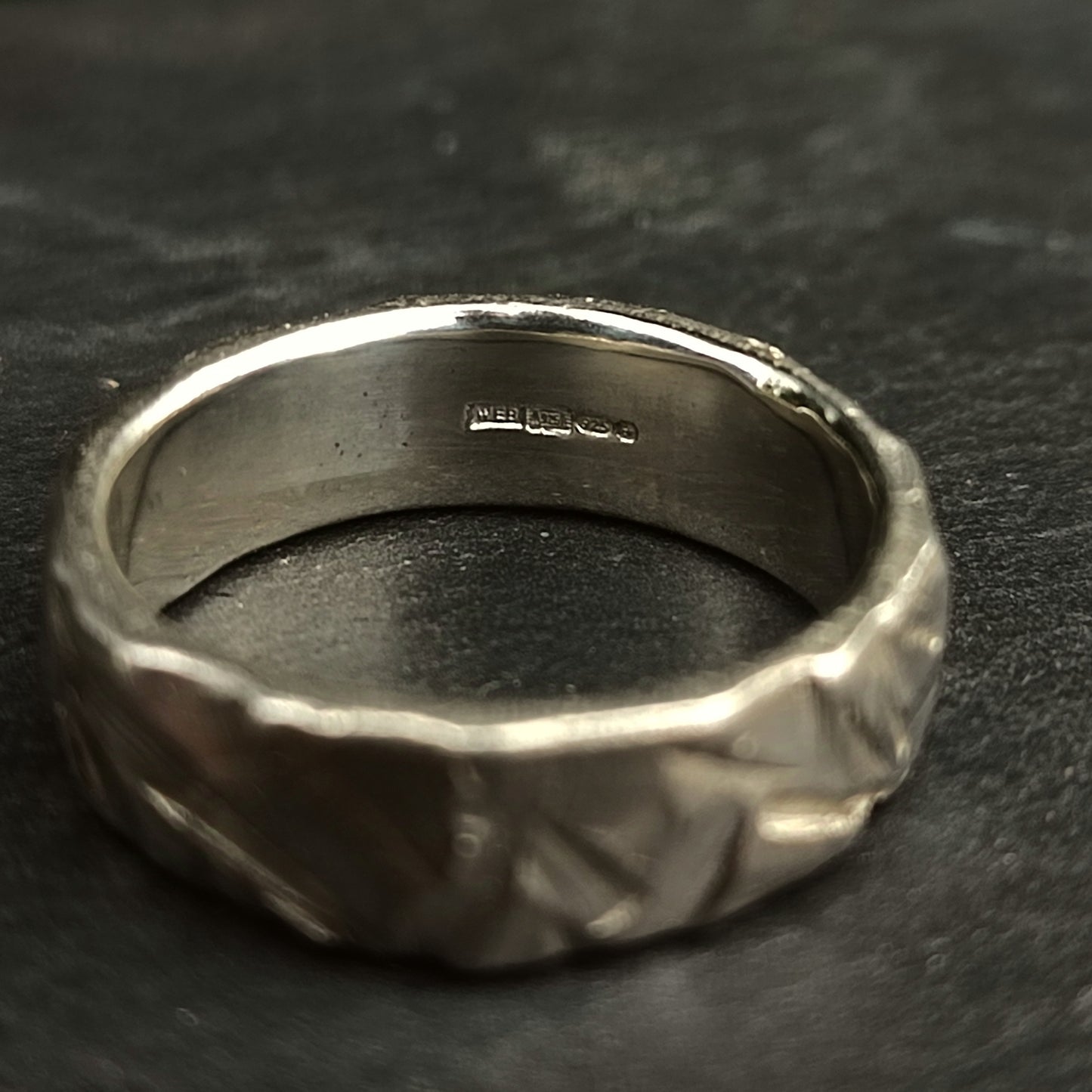 The Thick Rock Band by silverhollowjewellery is a chunky ring made from recycled 925 sterling silver, featuring a textured exterior and hallmark engravings inside, shown on a dark background.