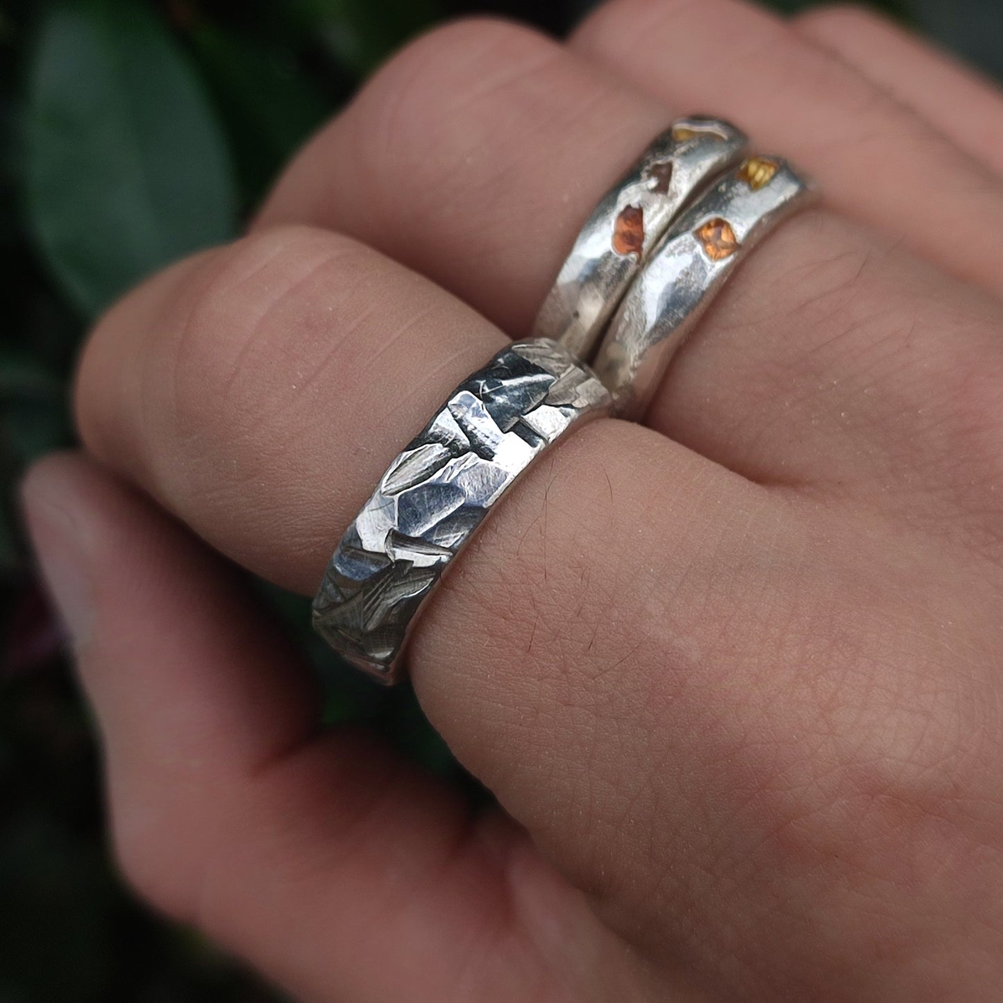 A hand wears two sterling silverhollowjewellery rings: the Thick Rock Band with a faceted, rock-textured design, and another band set with small amber-colored stones.