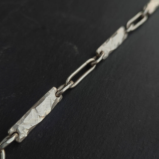 The Rock Bracelet by silverhollowjewellery is crafted from recycled sterling silver, showcasing alternating hammered rectangular and elongated oval links in a close-up view against a dark surface.