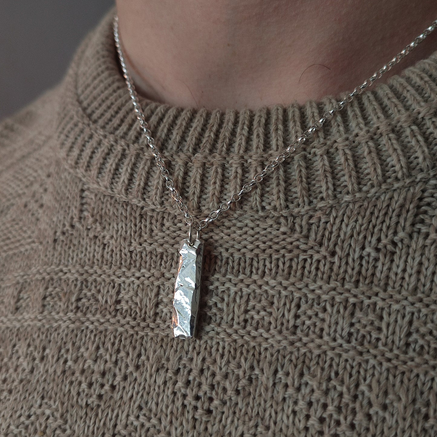 A close-up of a person wearing the silverhollowjewellery Rock Pendant, crafted from recycled sterling silver, on a chain necklace over a beige knitted sweater.