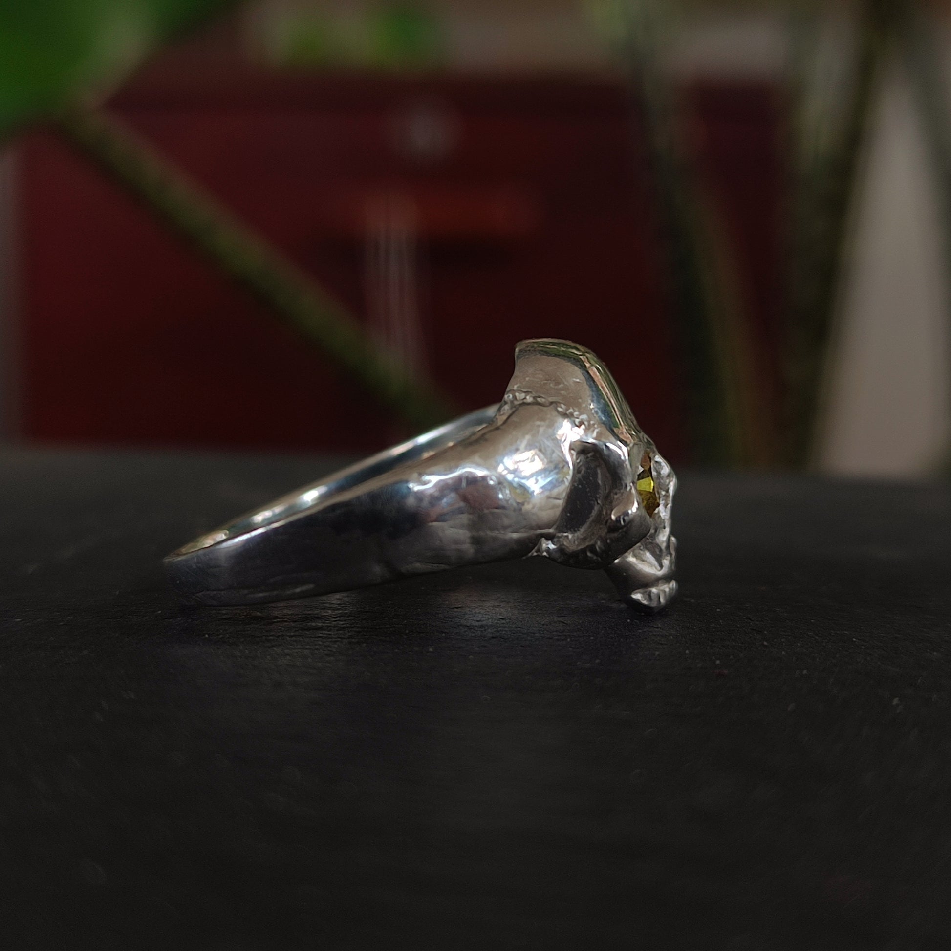 The yellow sapphire skull ring by silverhollowjewellery features a sculpted animal skull design in recycled sterling silver with detailed facial structure, showcased on a dark surface with a blurred background.