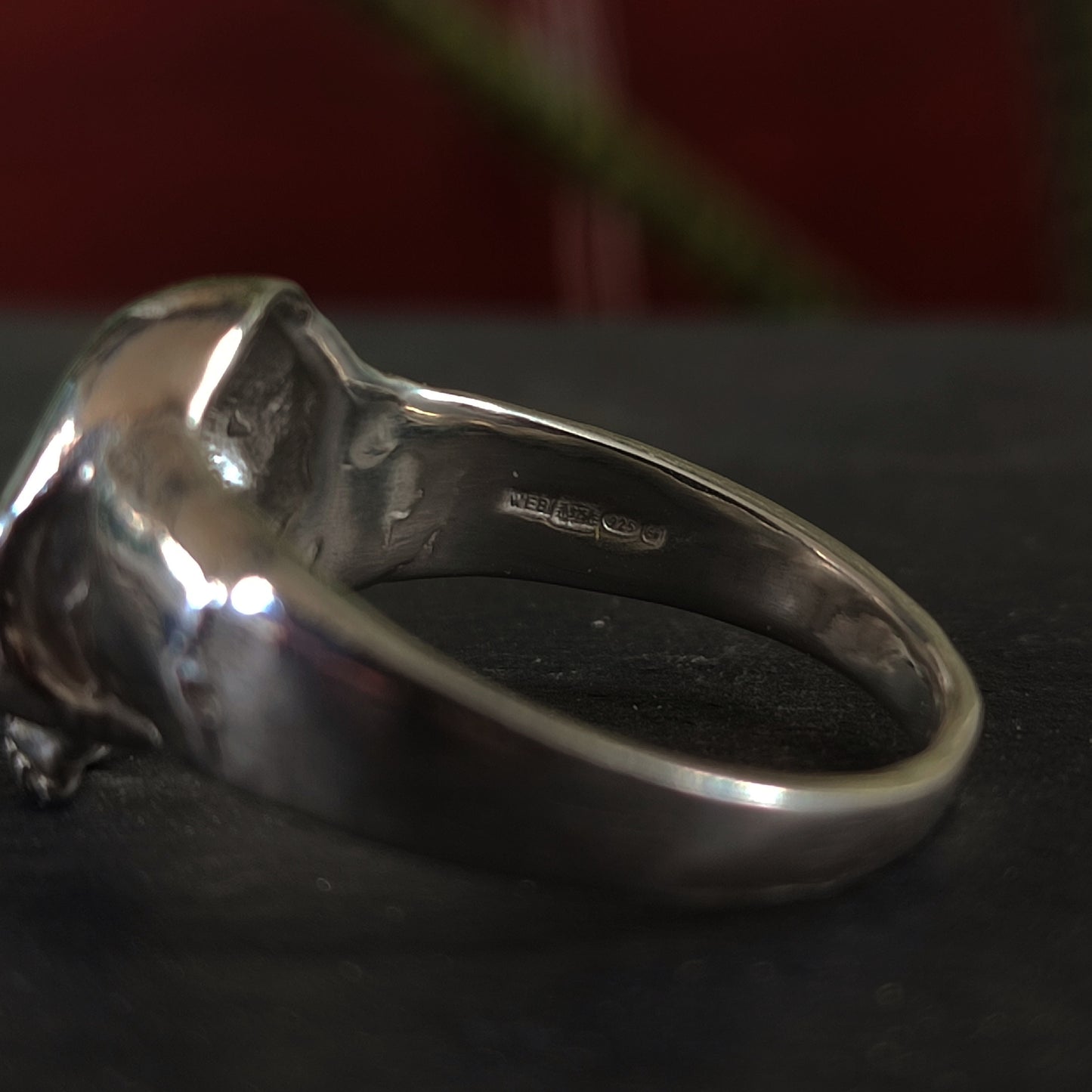 Close-up of the inner band of the silverhollowjewellery Yellow Sapphire Skull Ring, crafted from recycled sterling silver, featuring a hallmark stamp with several symbols against a dark, blurred background.