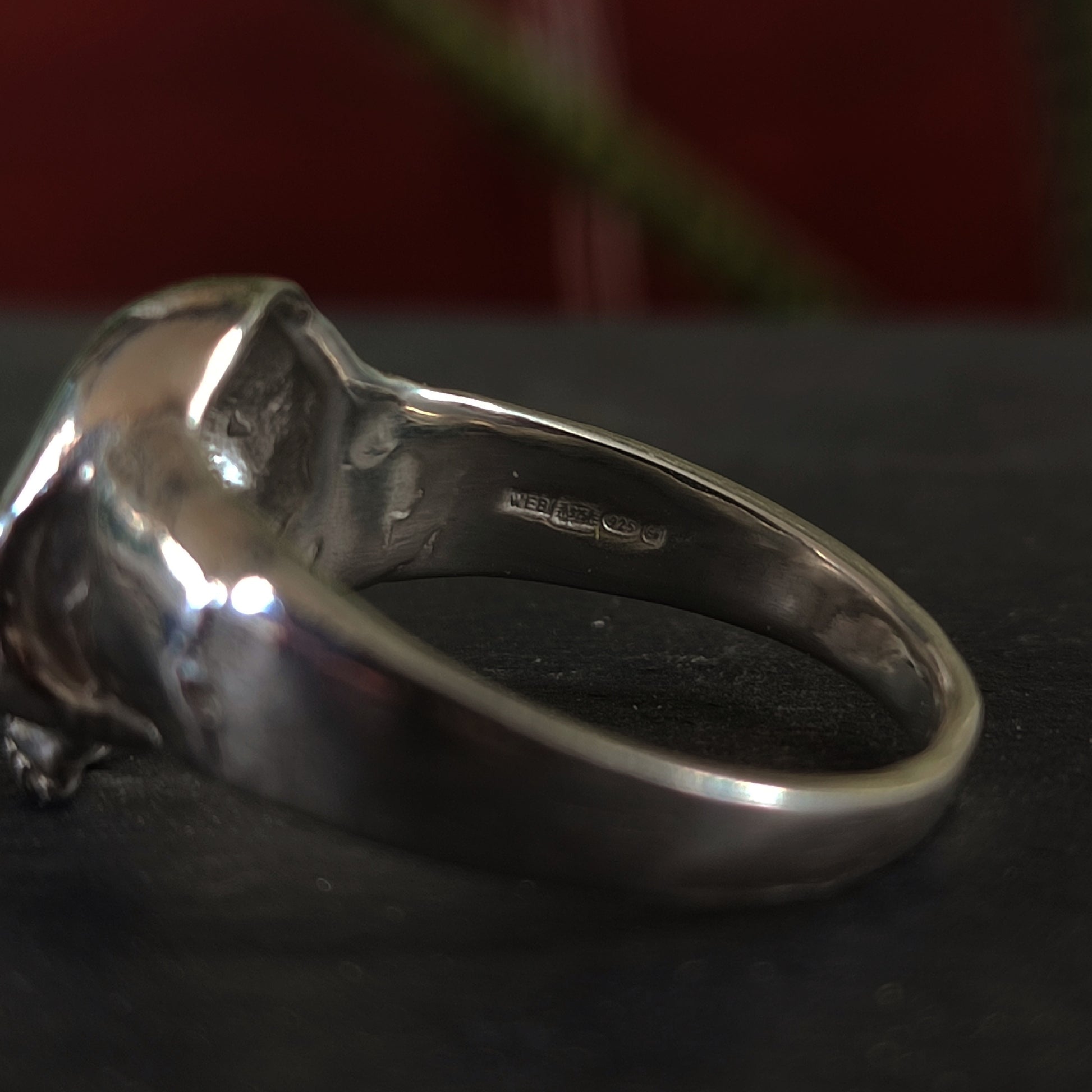 Close-up of the inner band of the silverhollowjewellery Yellow Sapphire Skull Ring, crafted from recycled sterling silver, featuring a hallmark stamp with several symbols against a dark, blurred background.
