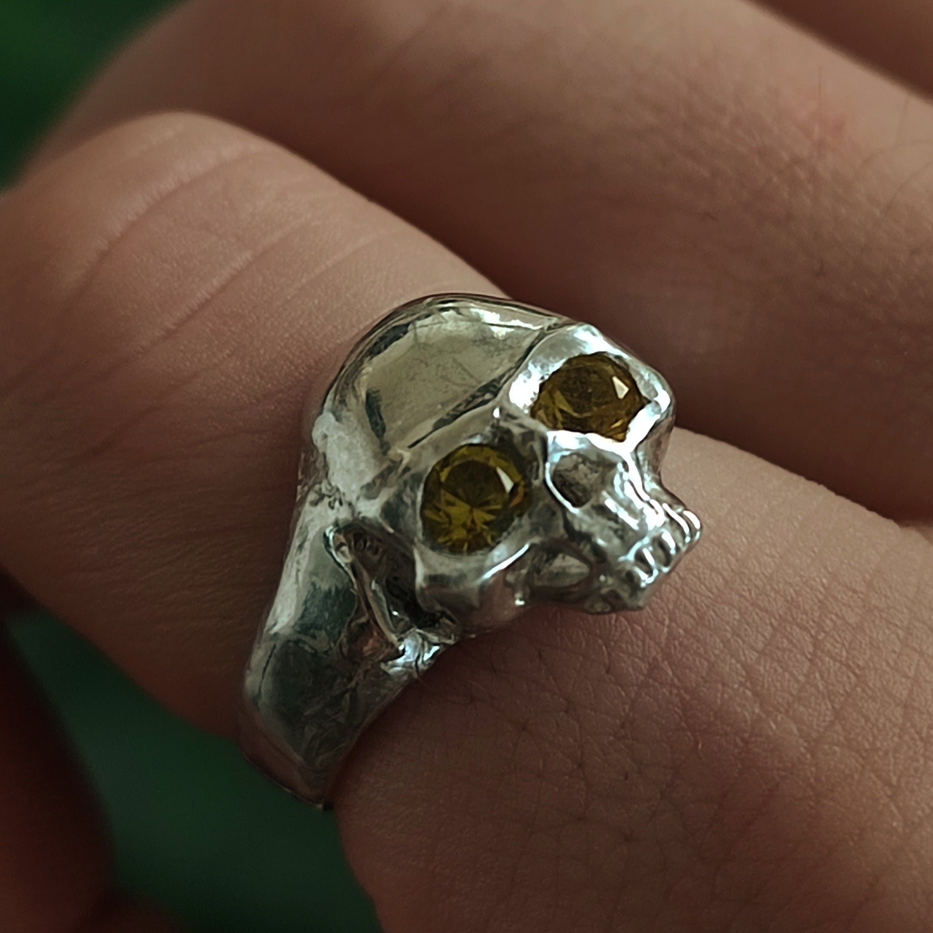 A close-up of silverhollowjewellery’s Yellow Sapphire Skull Ring, crafted from recycled sterling silver with yellow sapphire eyes, worn on a finger.