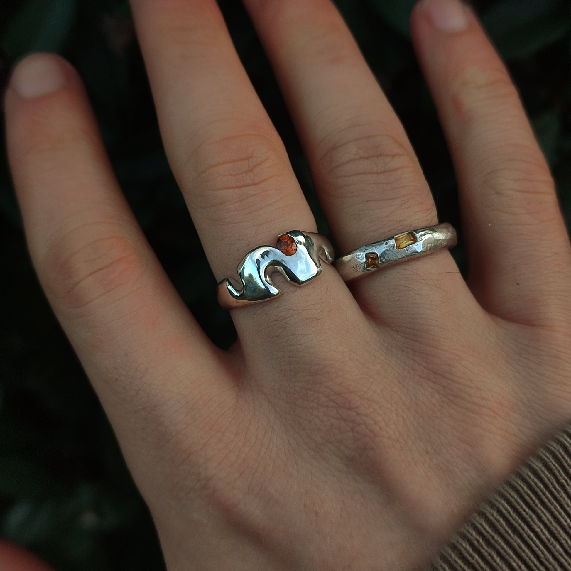A hand wearing the Sand Cast Sapphire Ring by silverhollowjewellery—crafted from recycled sterling silver—against a dark, blurred background.