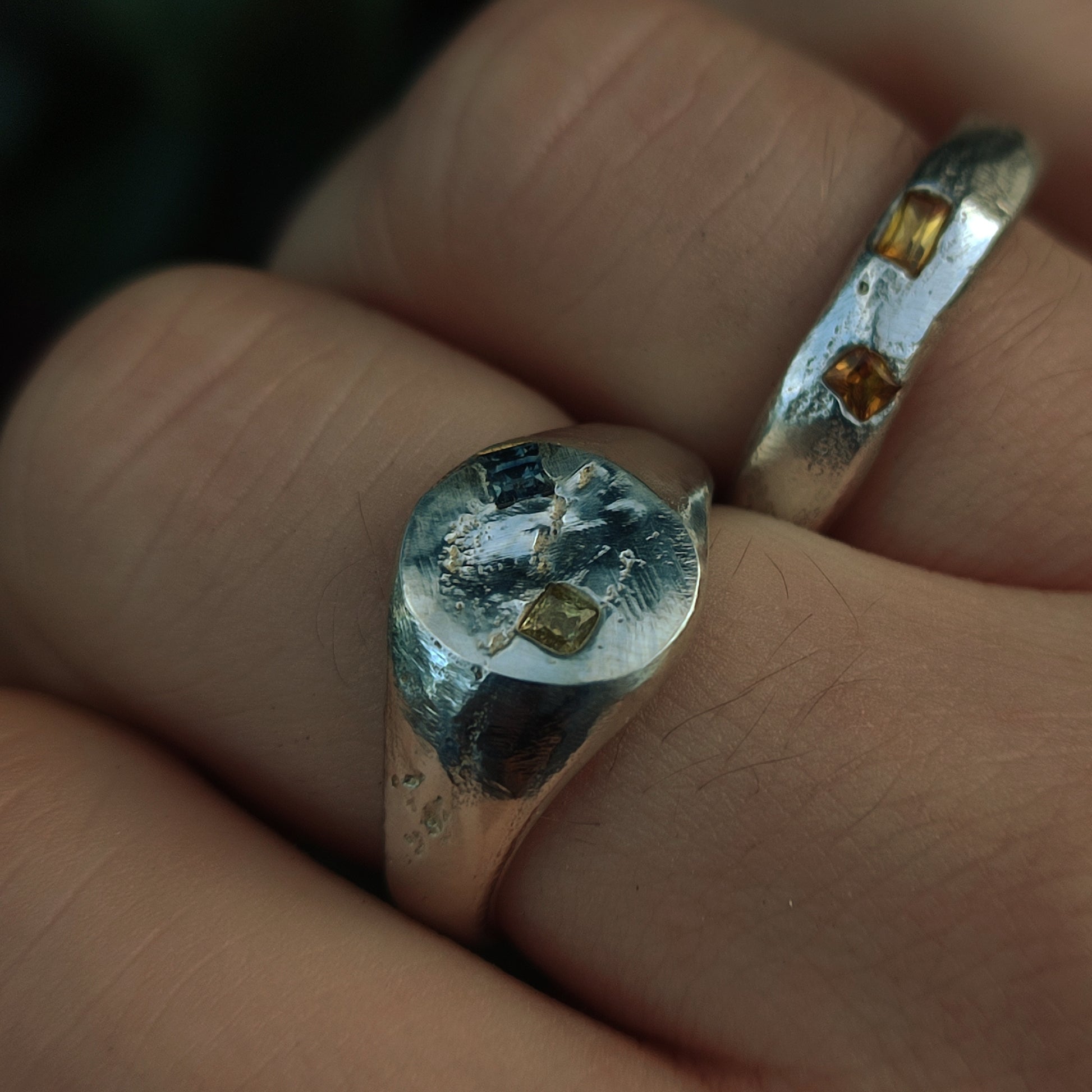 Close-up of two Sand Cast Sapphire Rings by silverhollowjewellery, handmade from recycled sterling silver with a textured finish and set with rectangular princess cut sapphires on a person's finger.