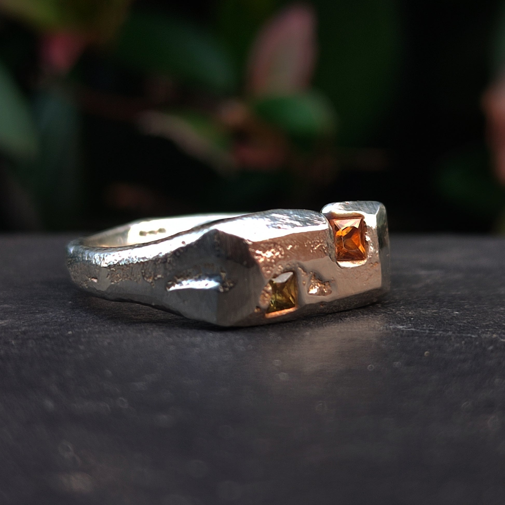 The Sand Cast Sapphire Ring by silverhollowjewellery is crafted from recycled sterling silver with a textured sand-cast finish and features two square yellow-orange princess cut sapphires in an angular design.