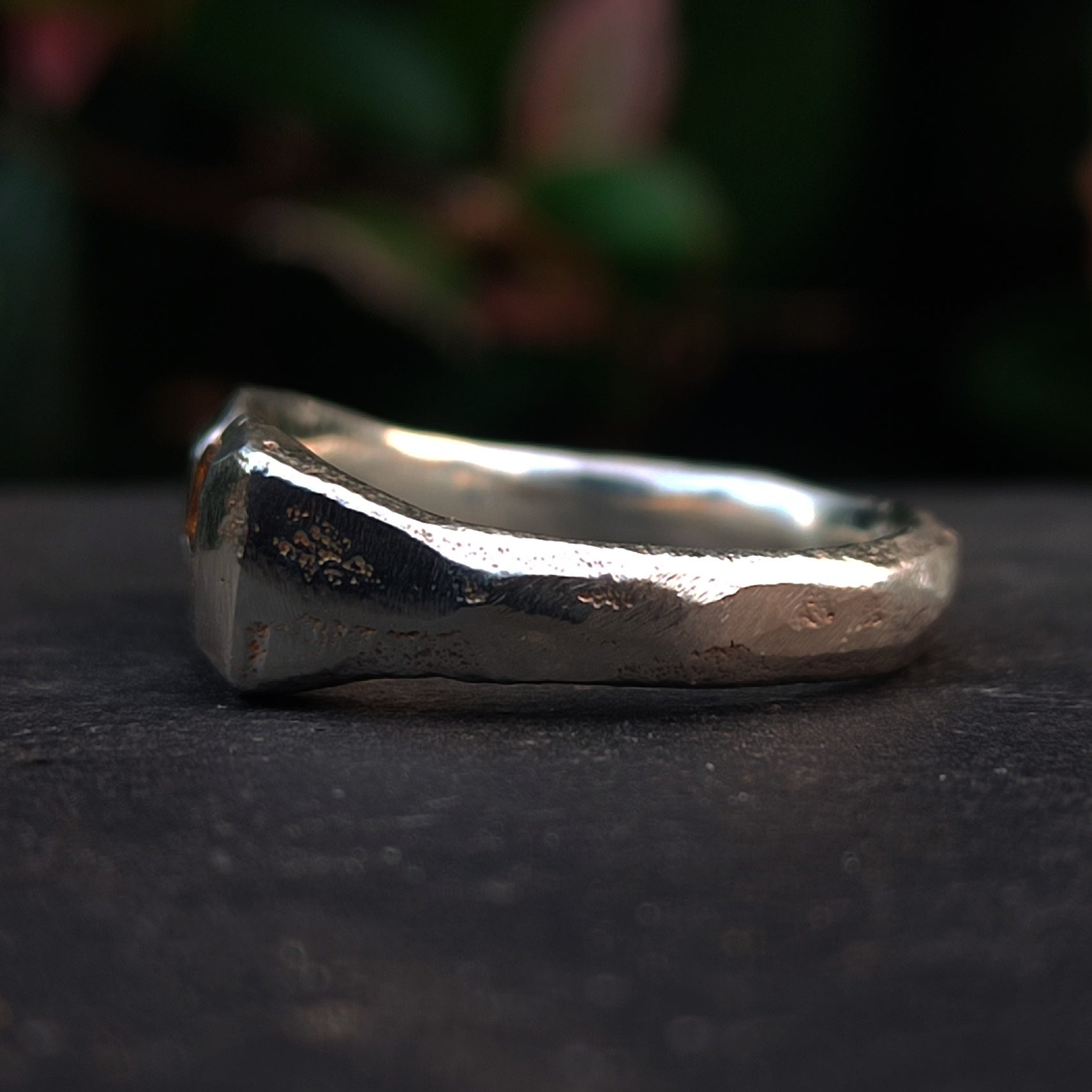 A close-up of the Sand Cast Sapphire Ring by silverhollowjewellery, featuring a chunky, irregular recycled sterling silver band with a hammered texture, set against a dark background.