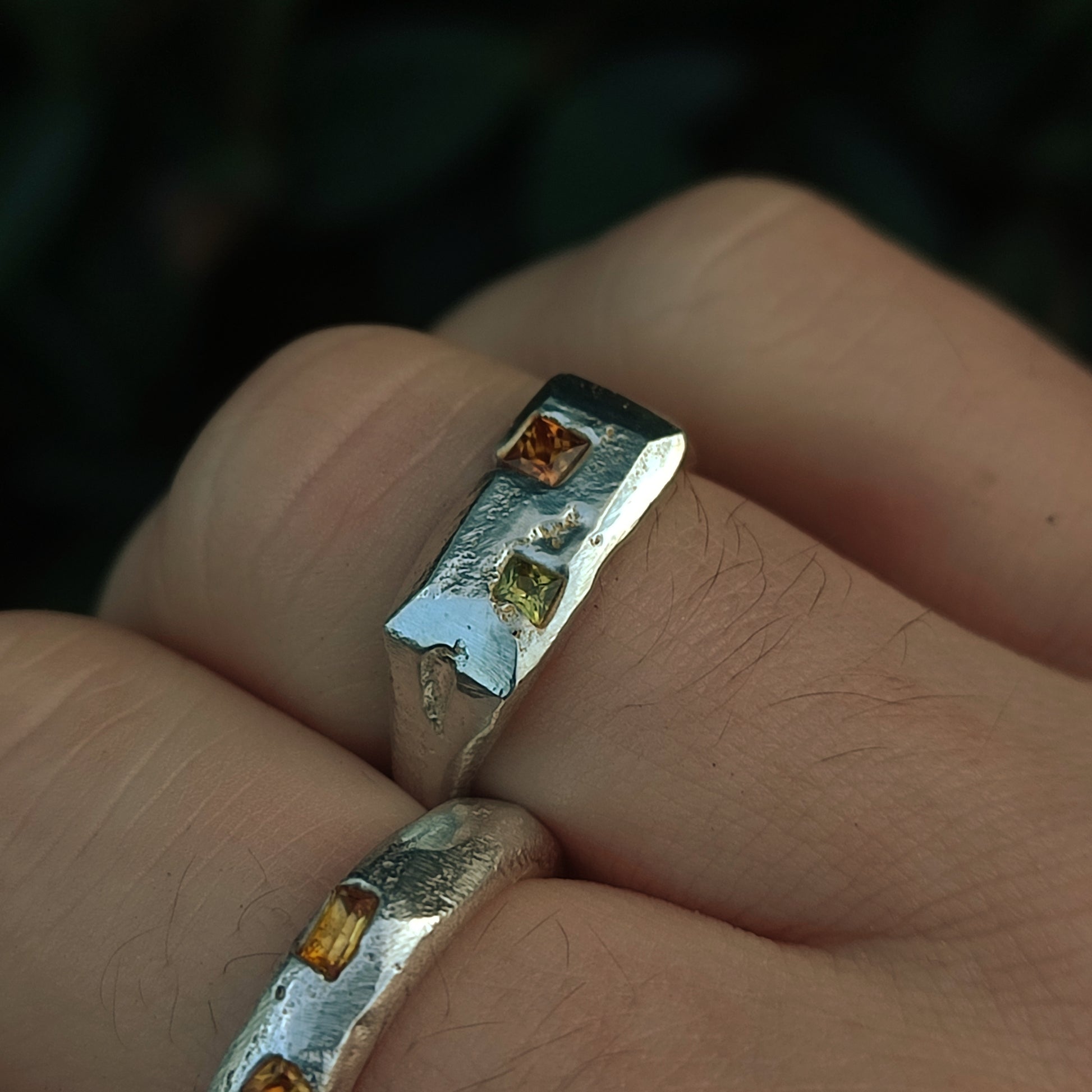 Close-up of the Sand Cast Sapphire Ring by silverhollowjewellery, featuring recycled sterling silver and three princess cut sapphires—two yellow and one light green—shown worn on a finger.
