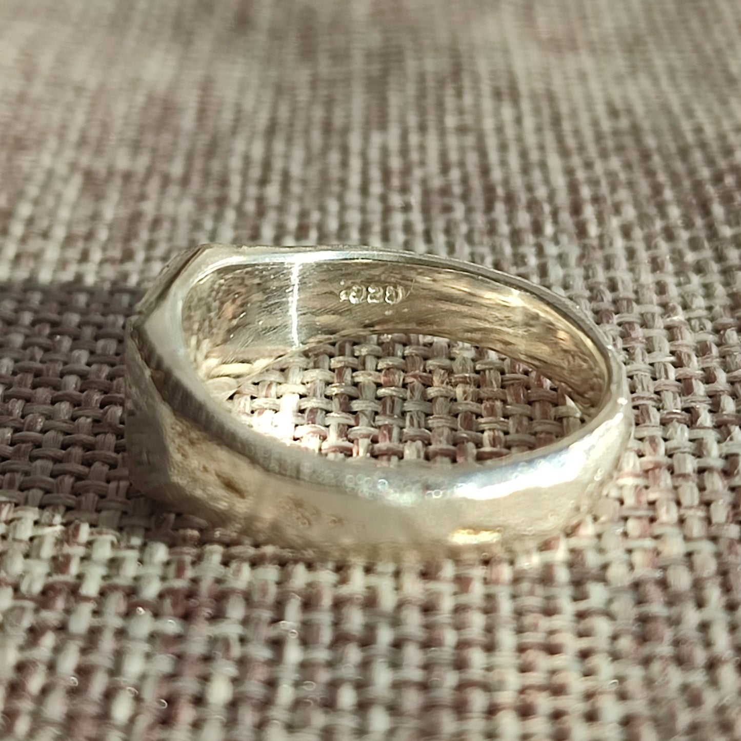 The Sand Cast Sapphire Signet by silverhollowjewellery, crafted from recycled sterling silver, rests on woven fabric and displays the “925” hallmark inside the band.