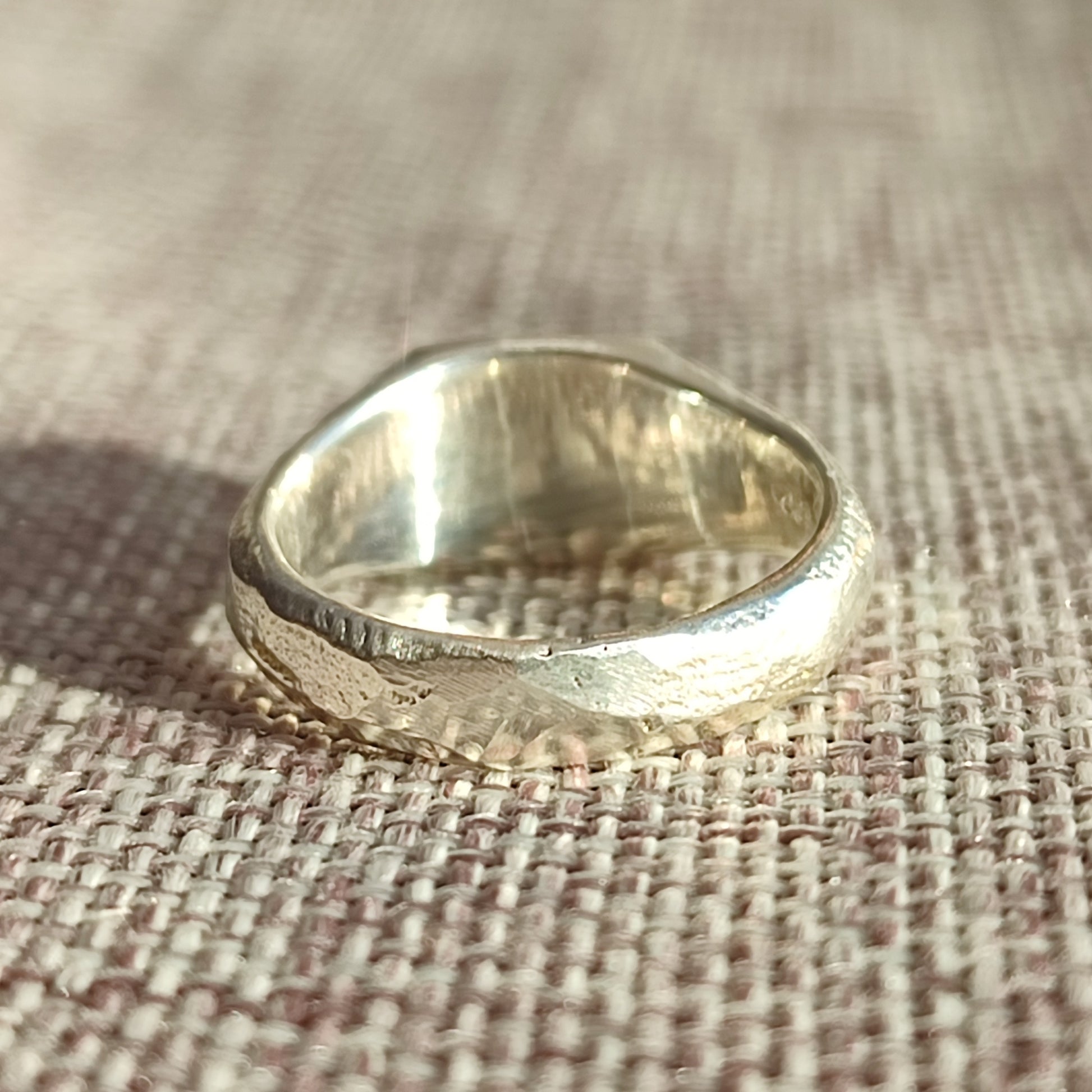 The Sand Cast Sapphire Signet by silverhollowjewellery, crafted from recycled sterling silver with a hammered finish, rests on woven beige fabric and is illuminated by natural light.