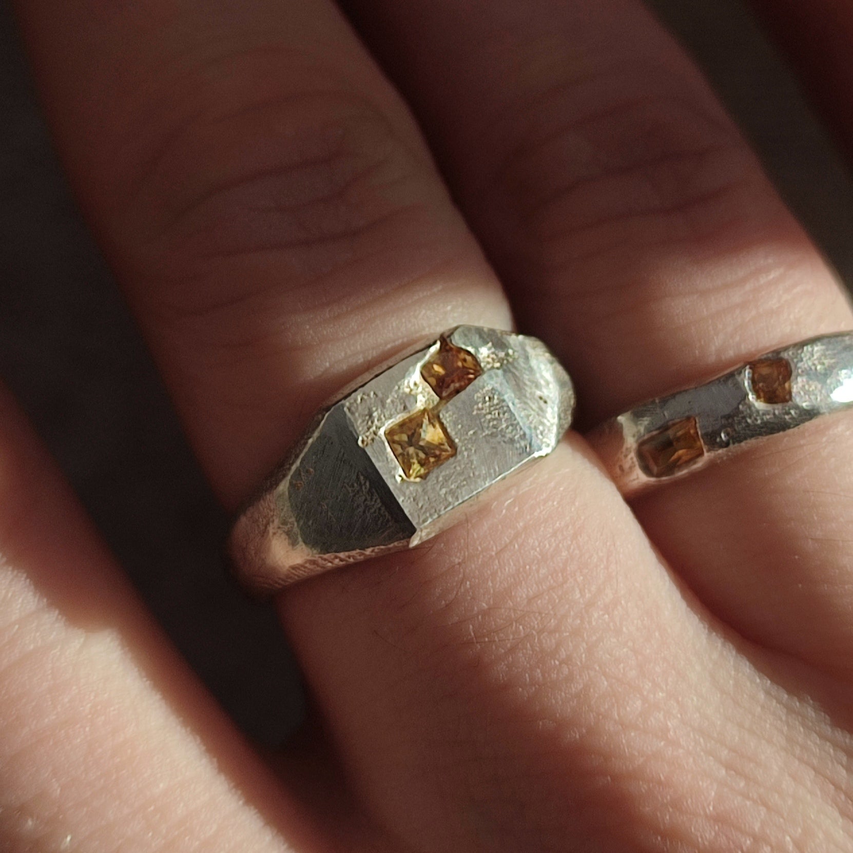 Close-up of two Sand Cast Sapphire Signet rings by silverhollowjewellery, crafted from recycled sterling silver and set with small square princess cut sapphires on each finger.