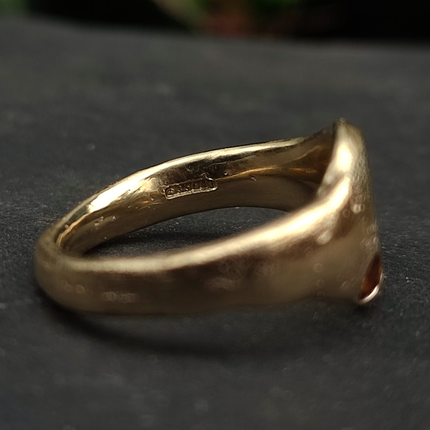 A close-up of the 9ct Sandcast Sapphire Signet by silverhollowjewellery, featuring a smooth, handcrafted recycled gold band with a visible hallmark on the inner side, resting on a dark surface.