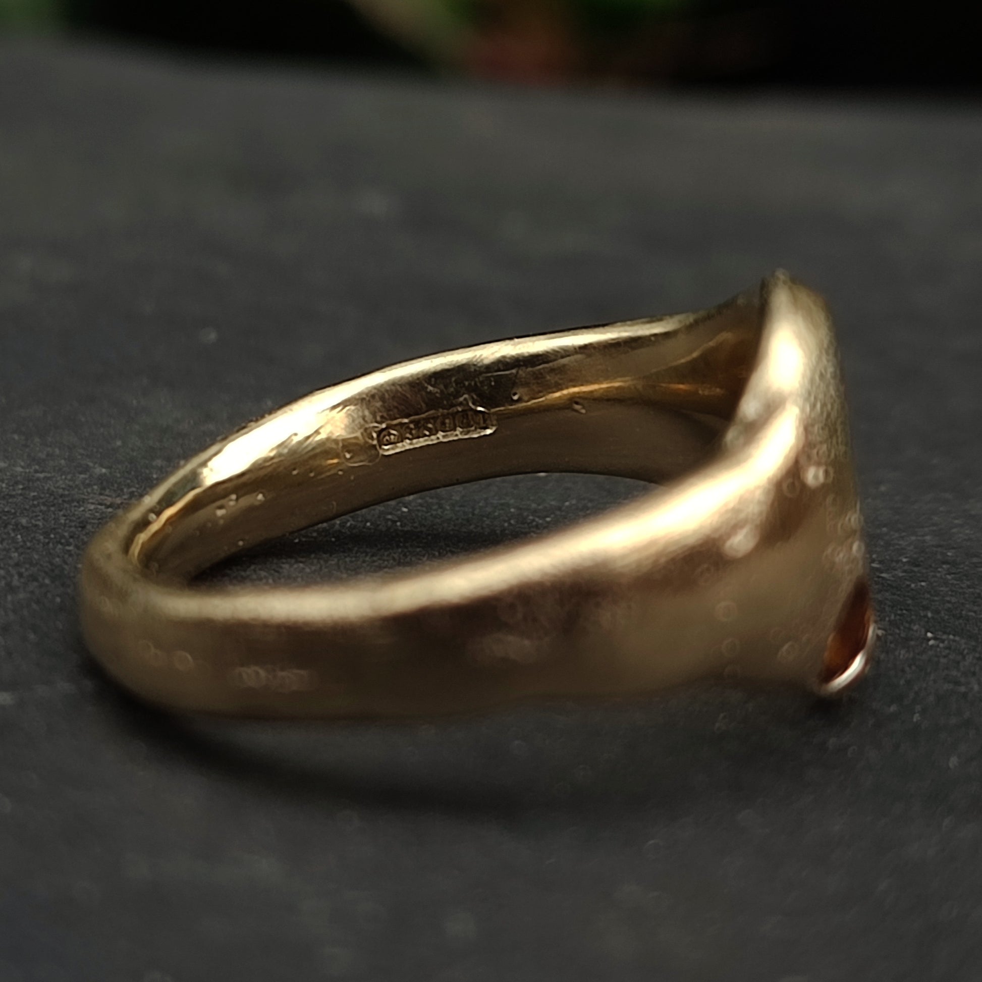 A close-up of the 9ct Sandcast Sapphire Signet by silverhollowjewellery, featuring a smooth, handcrafted recycled gold band with a visible hallmark on the inner side, resting on a dark surface.