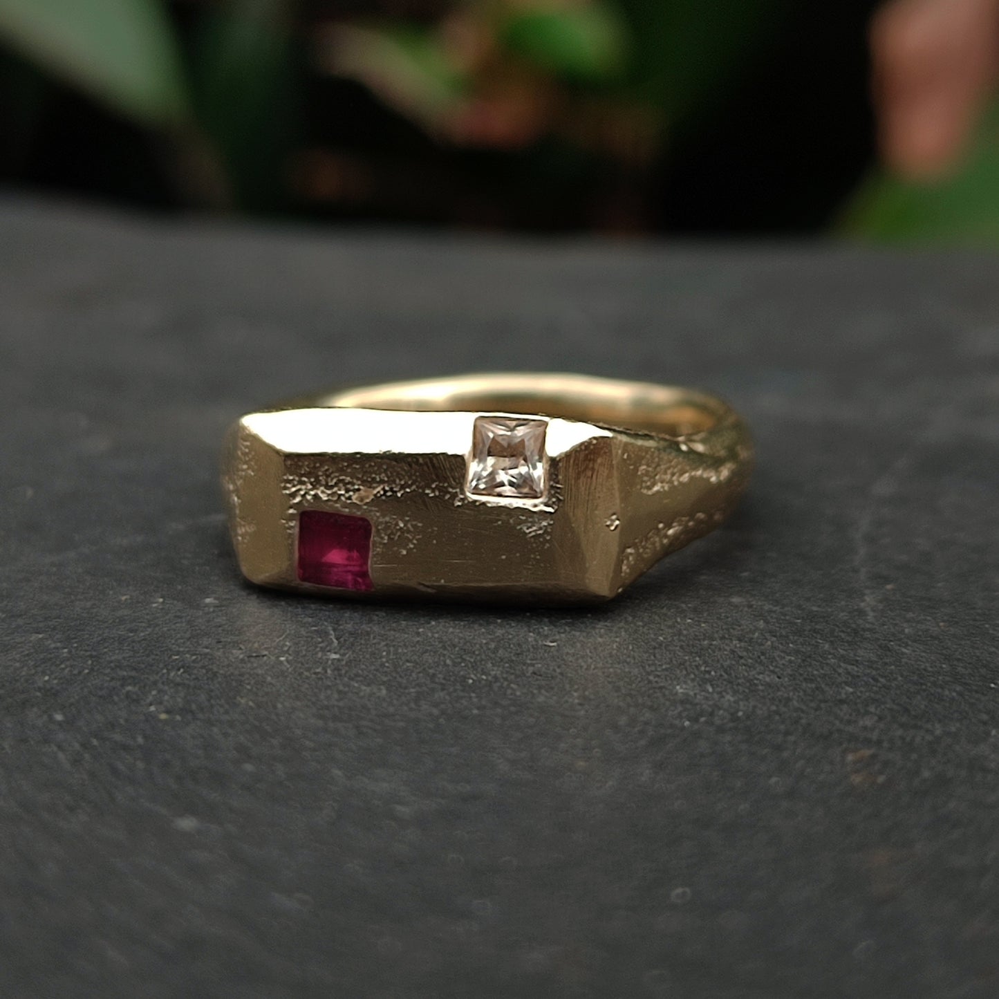The 9ct Sandcast Sapphire/Ruby Signet by silverhollowjewellery is a recycled gold ring with a textured finish, showcasing a square red ruby and a square white sapphire set side by side on top.