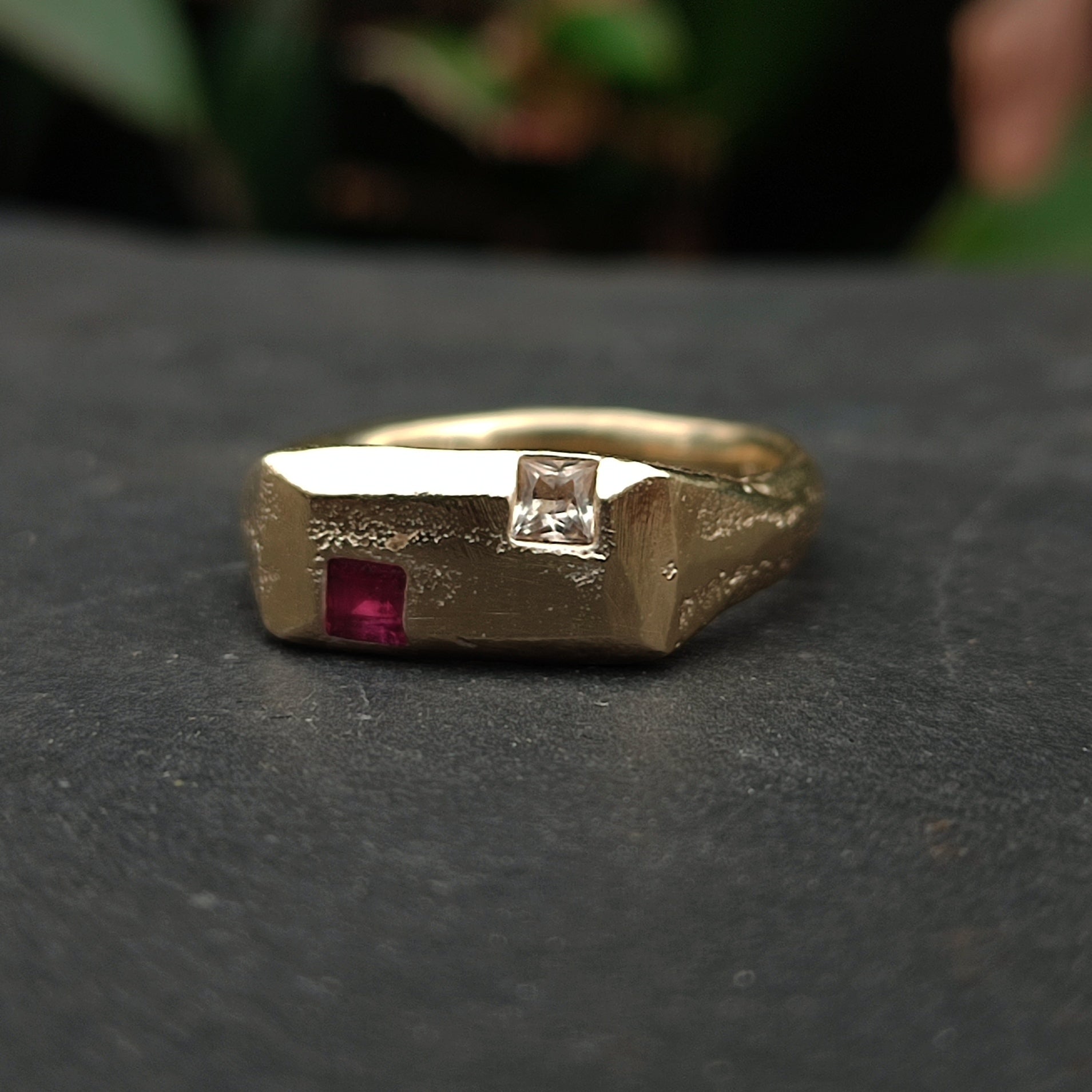 The 9ct Sandcast Sapphire/Ruby Signet by silverhollowjewellery is a recycled gold ring with a textured finish, showcasing a square red ruby and a square white sapphire set side by side on top.
